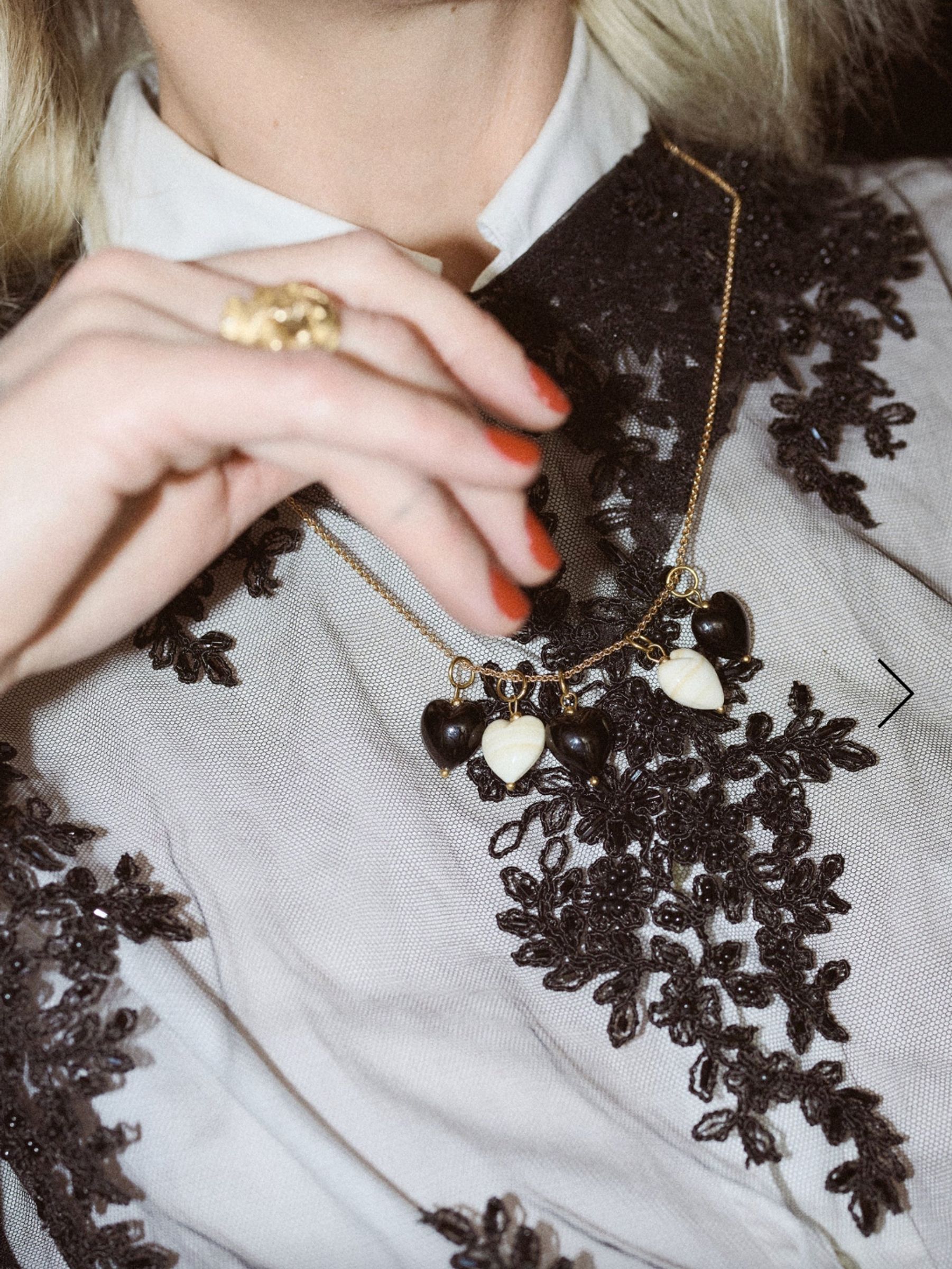 woman wears heart pendant necklace over a sheer black top with black lace detailing
