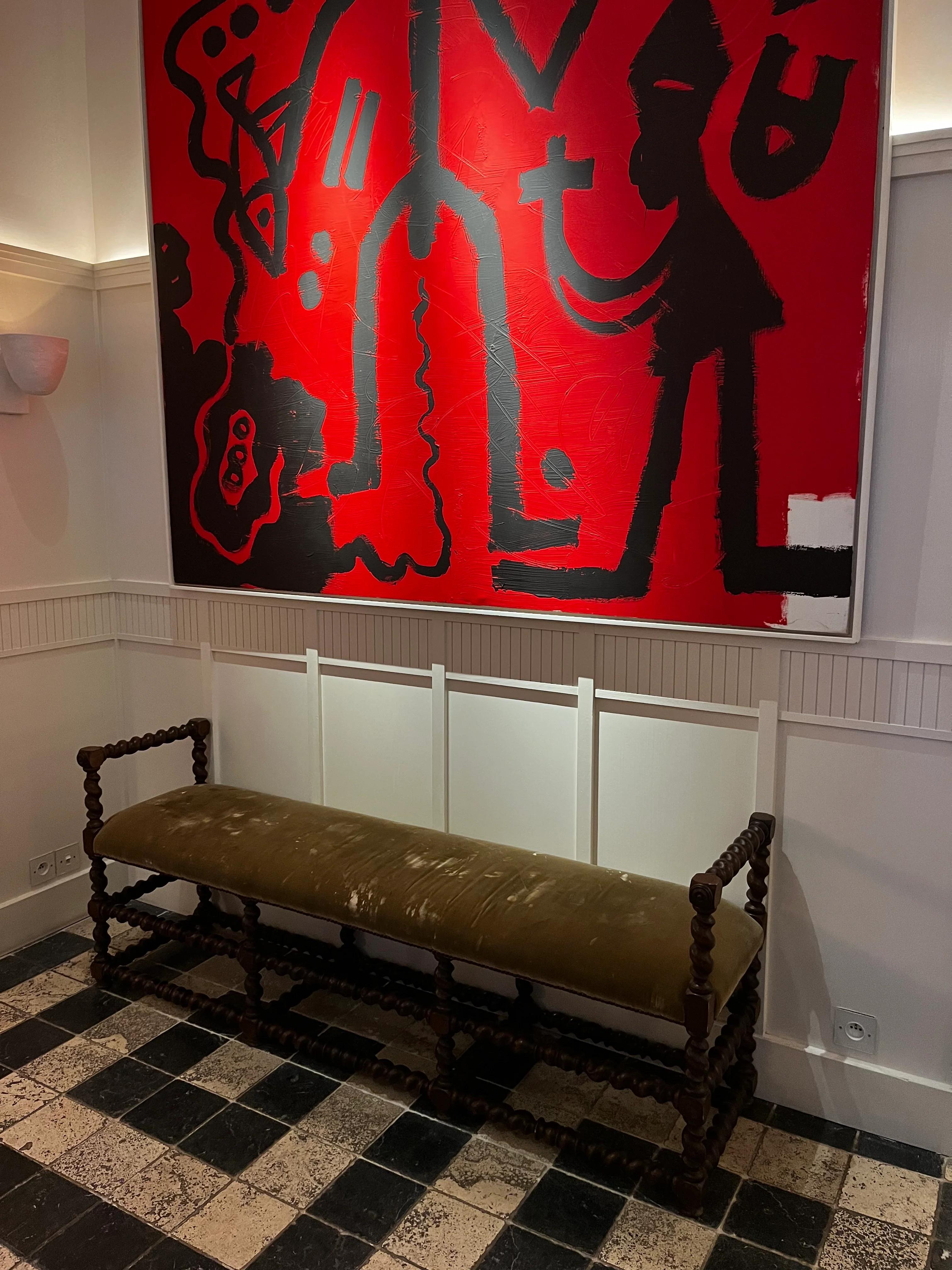 Hallway with long wooden bench and green cushion. Large abstract red and black painting behind. Checkered floor tiles.