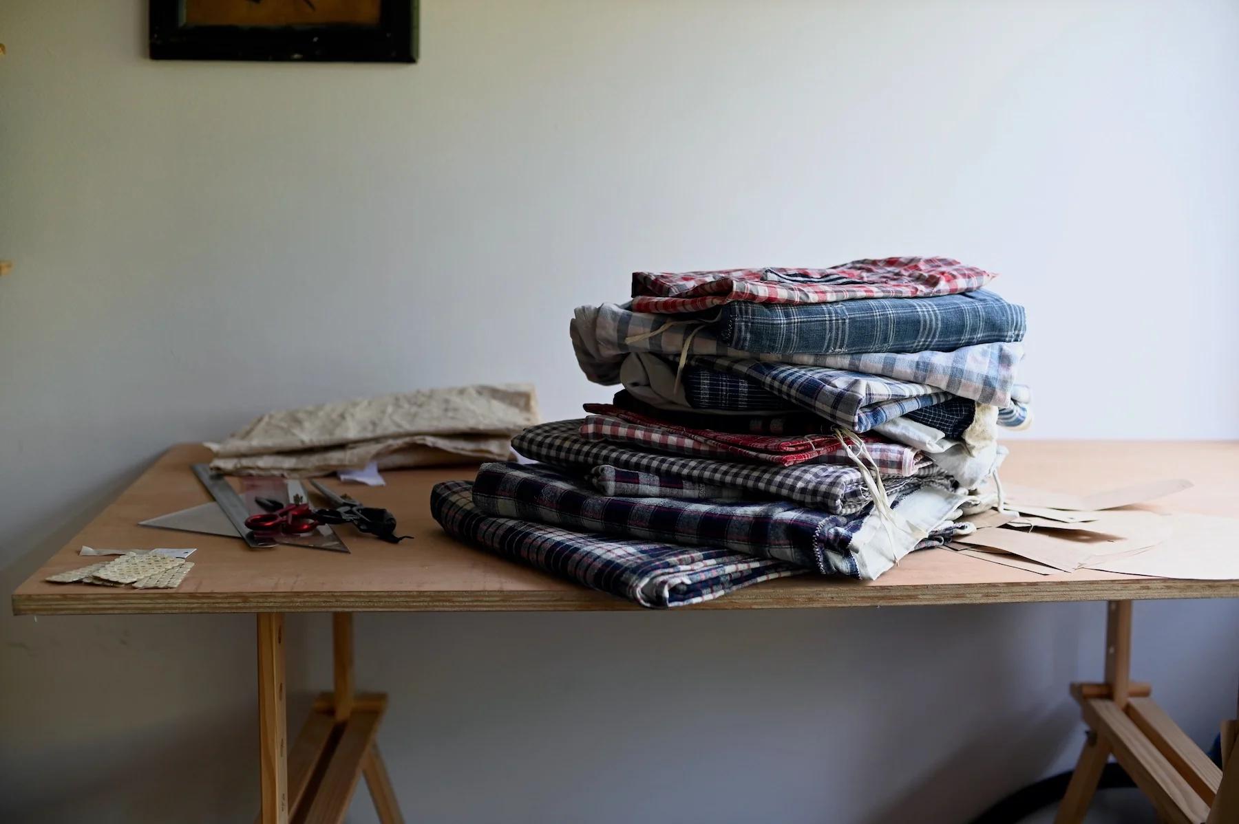 Folded checkered fabrics on wooden table. Scissors and paper patterns scattered around.