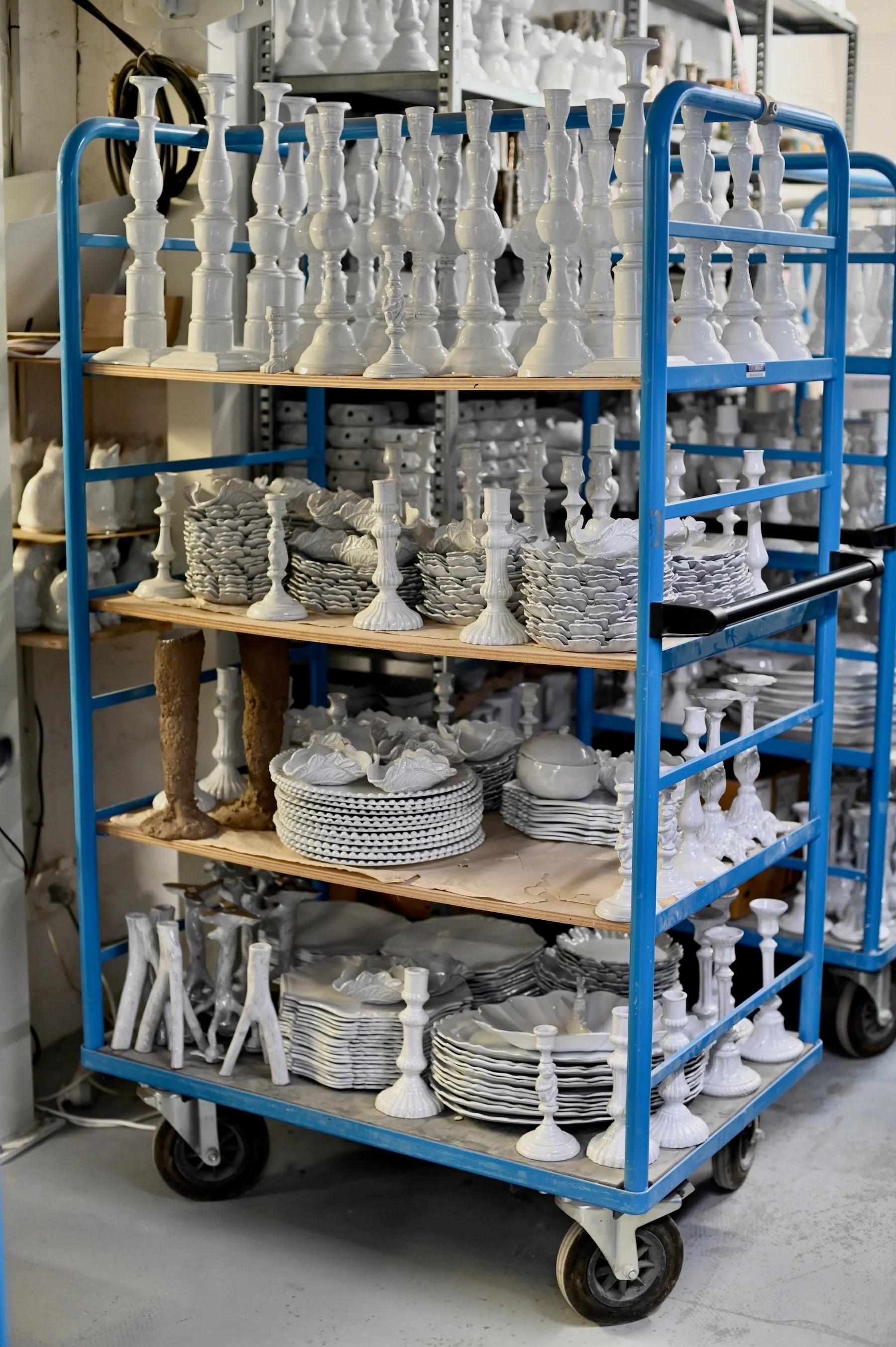 Two individuals organizing white ceramic plates and dishes on wooden table covered with brown paper. Shopping cart in background.