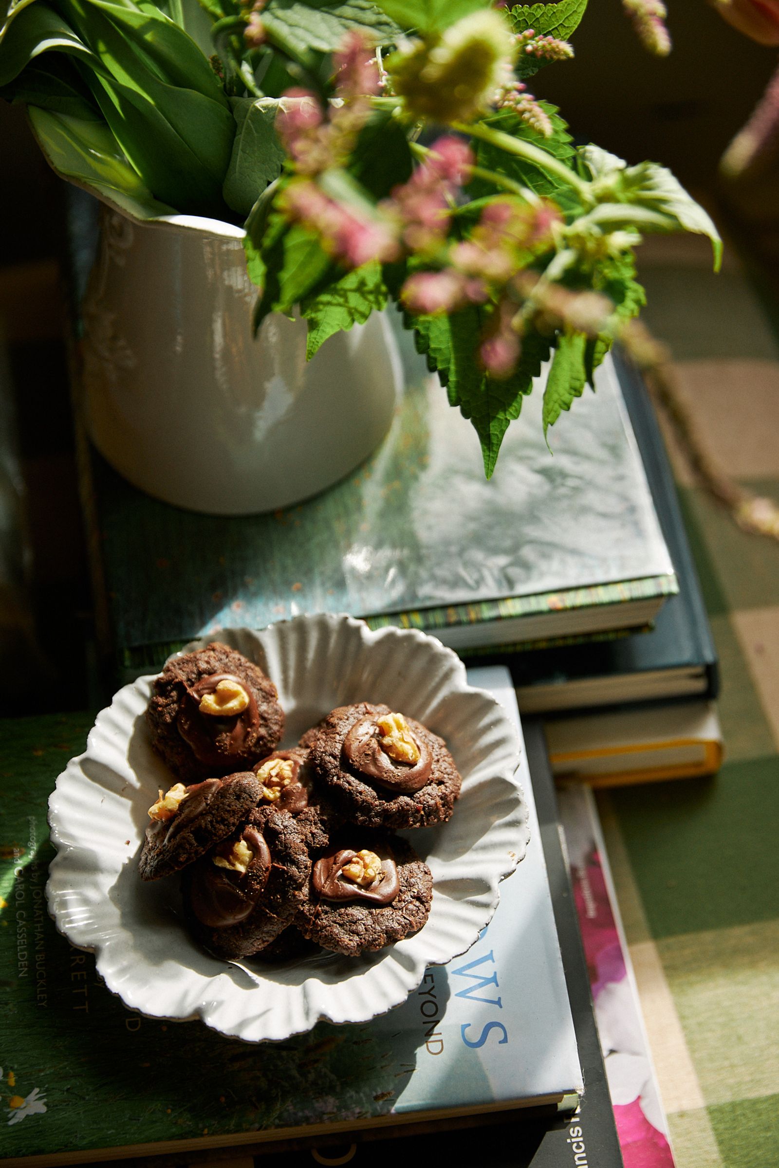 afgan cookies on a white plate next to a vase of flowers and books
