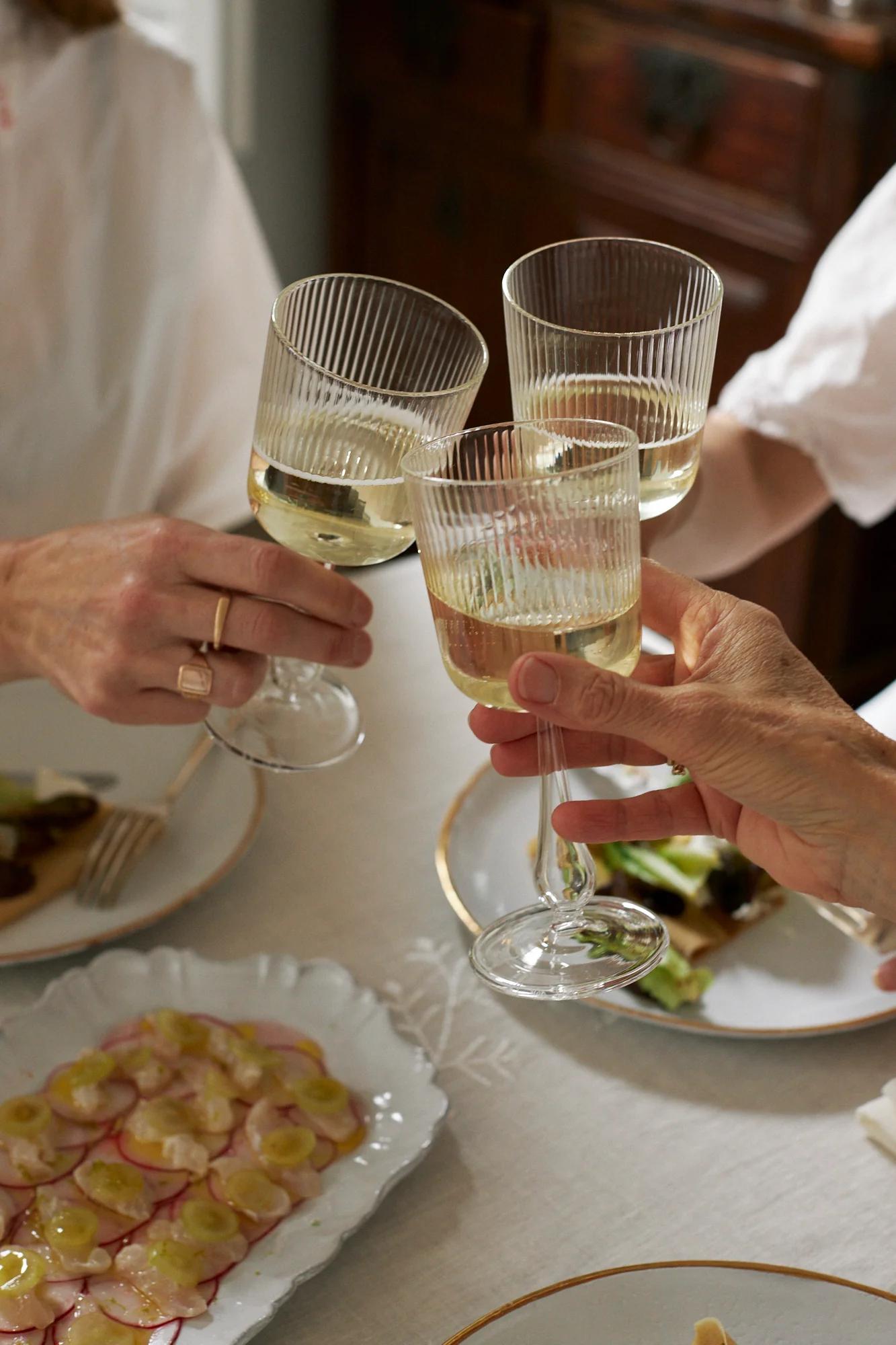 Three people toast with white wine over a table of food, including fresh ceviche on radish slices. The scene captures a joyous celebration.