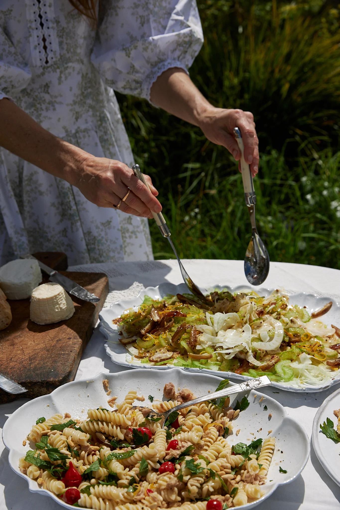 hands serve salad from two large platters set on a table 