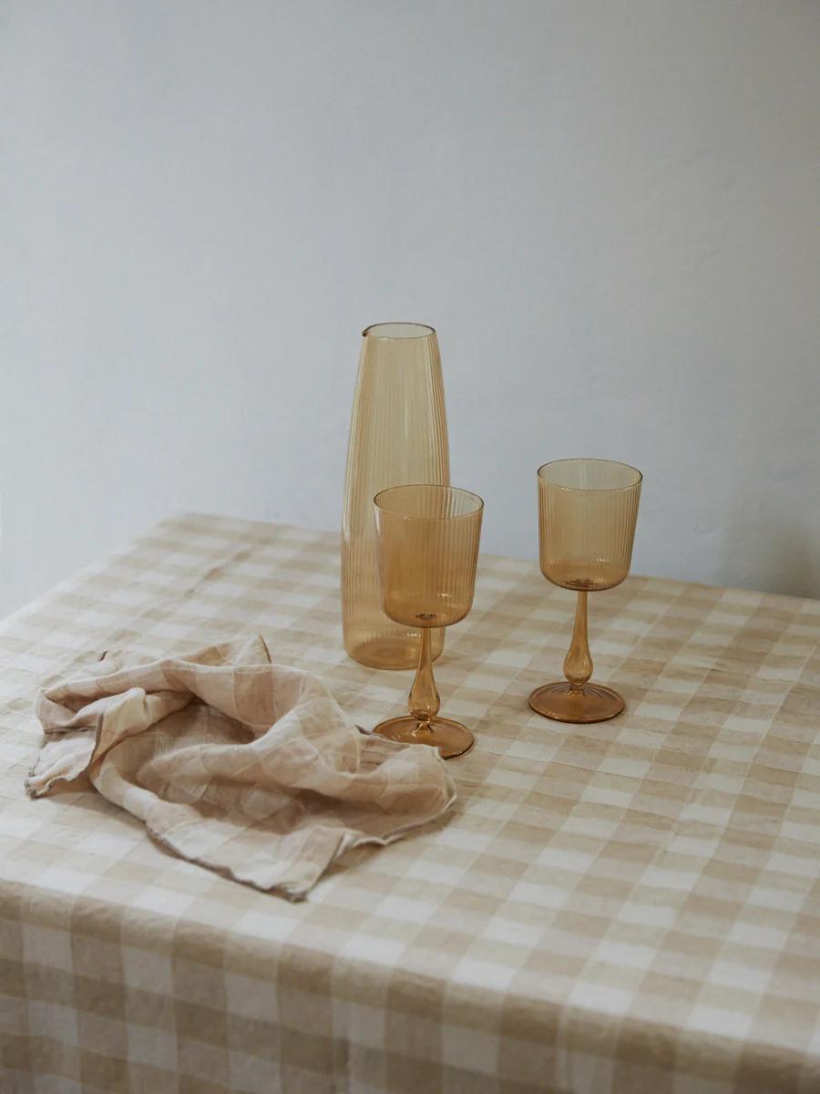 Table set with checkered tablecloth, amber goblets, tall vase. Soft lighting, minimalist decor.