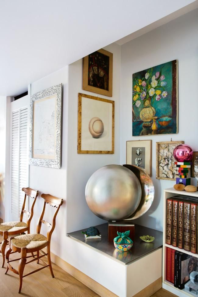 Cozy corner with eclectic gallery wall. Niche displays decorative items. Two wooden chairs with woven seats nearby.