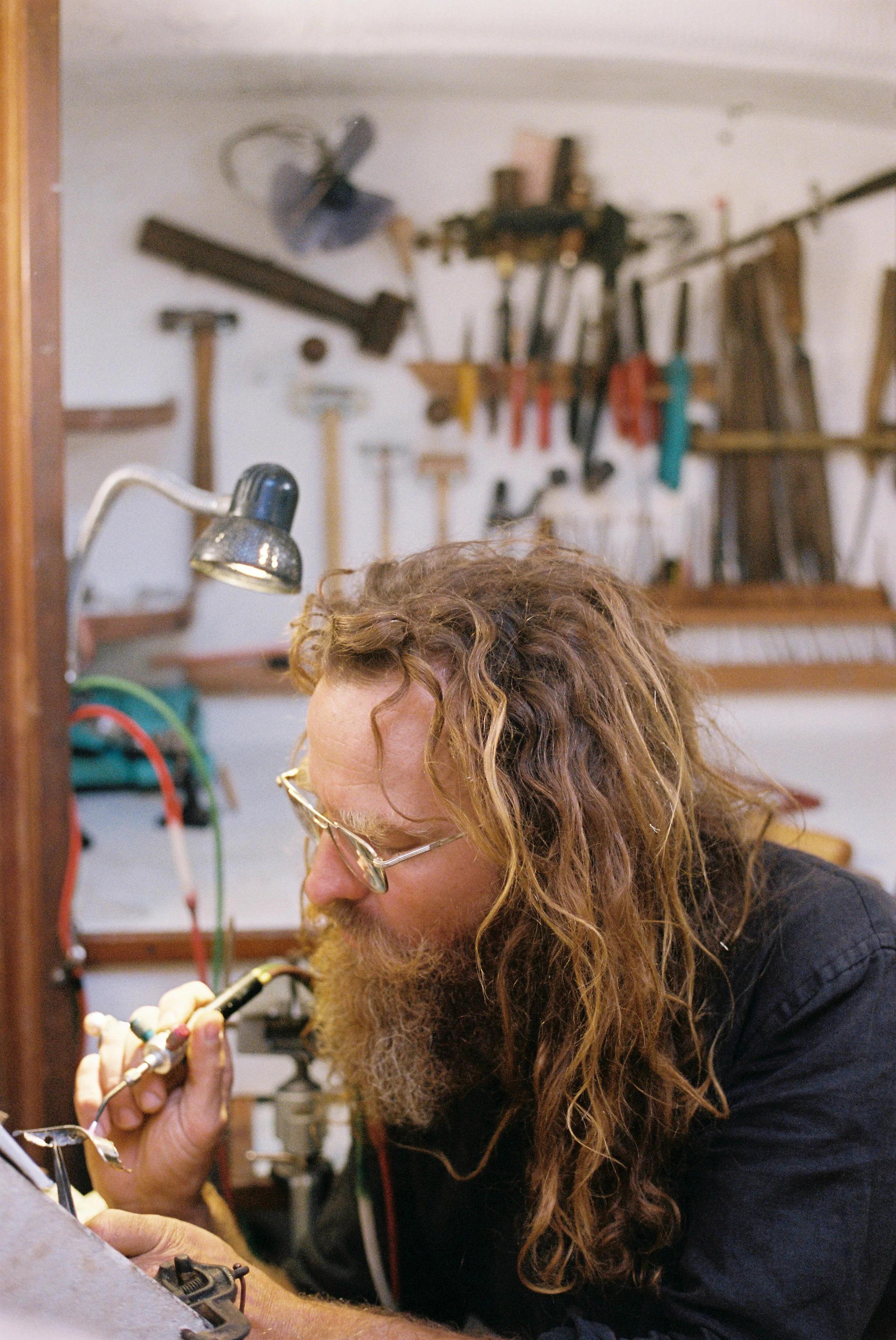 Person using soldering tool at workbench. Tools and equipment on wall behind.