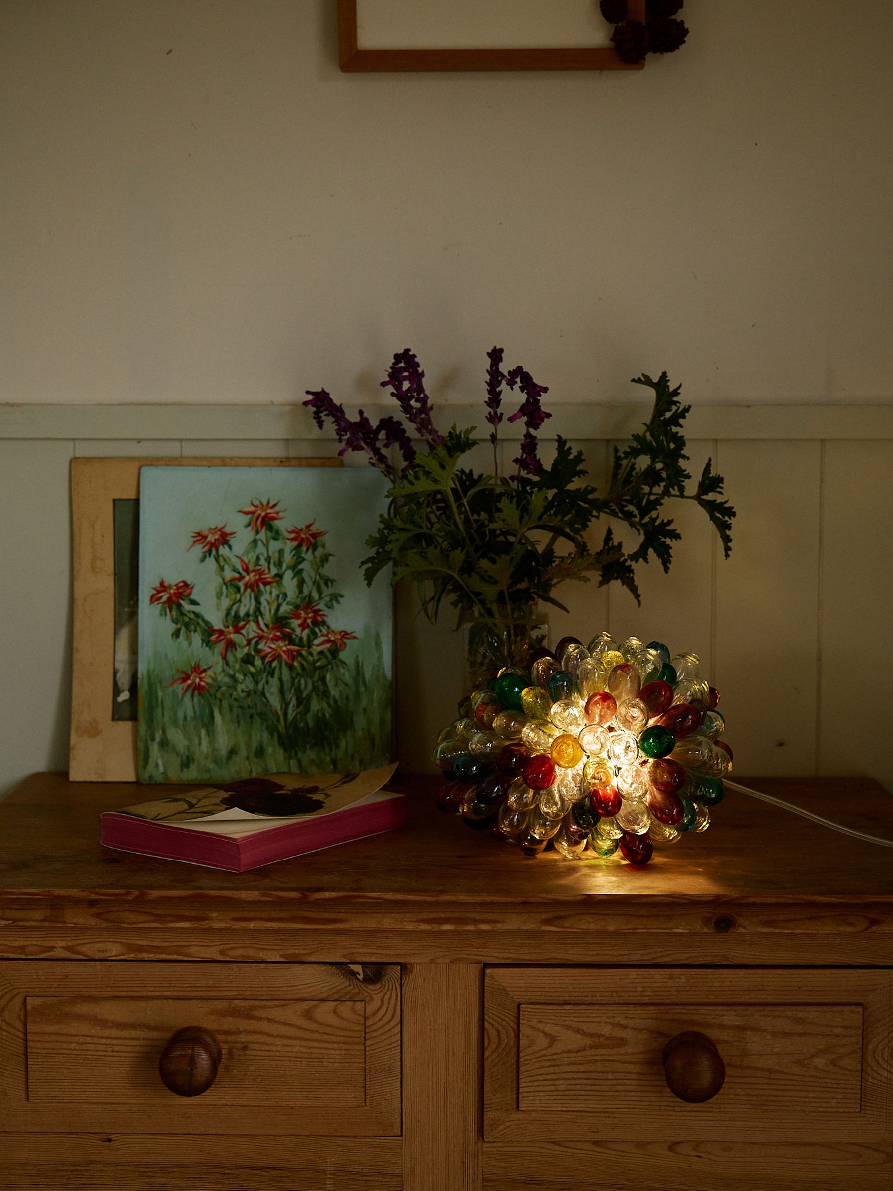 multi coloured lamp sits on side table with books and flowers
