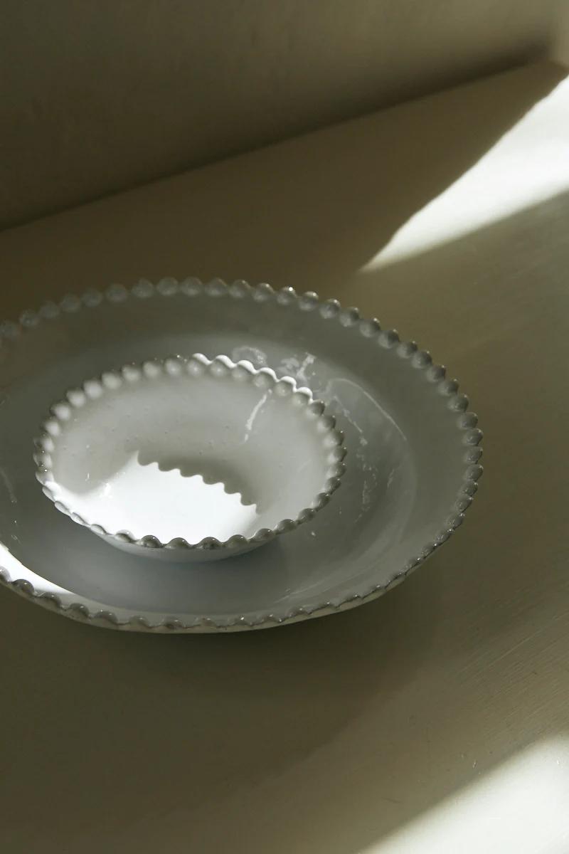 Small white ceramic bowl inside larger bowl. Beaded edges. Light surface, sunlight casting contrasting shadows.