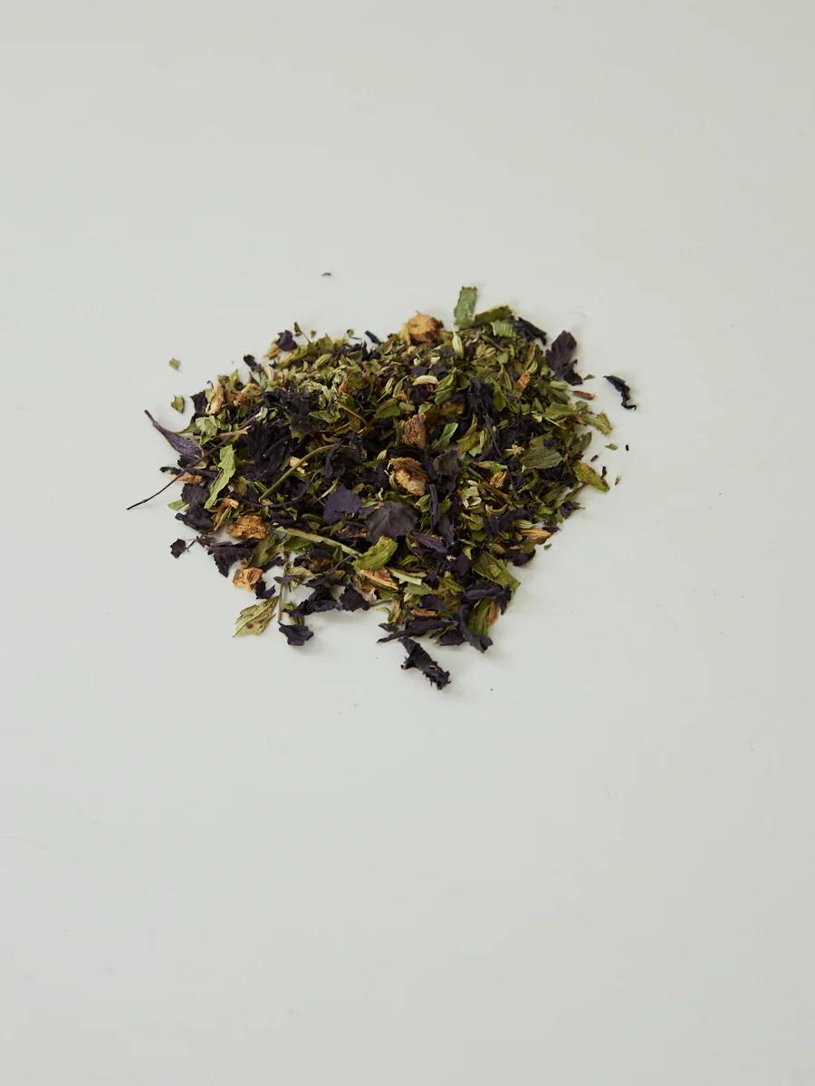 Small pile of loose leaf herbal tea on light gray background. Various green, brown, and purple dried leaves.