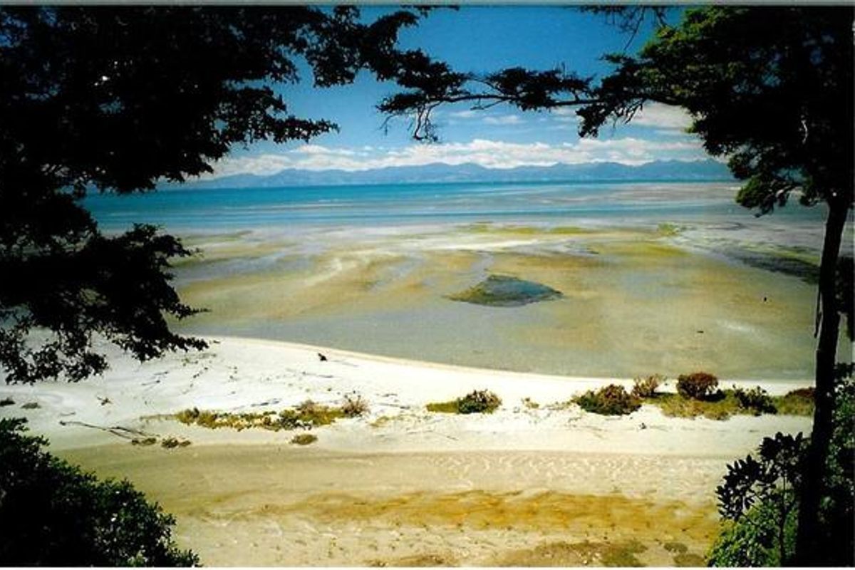 Panoramic beach view: white sand, greenery, shallow blue waters. Distant mountains under blue sky with scattered clouds inspire nature-themed designs.