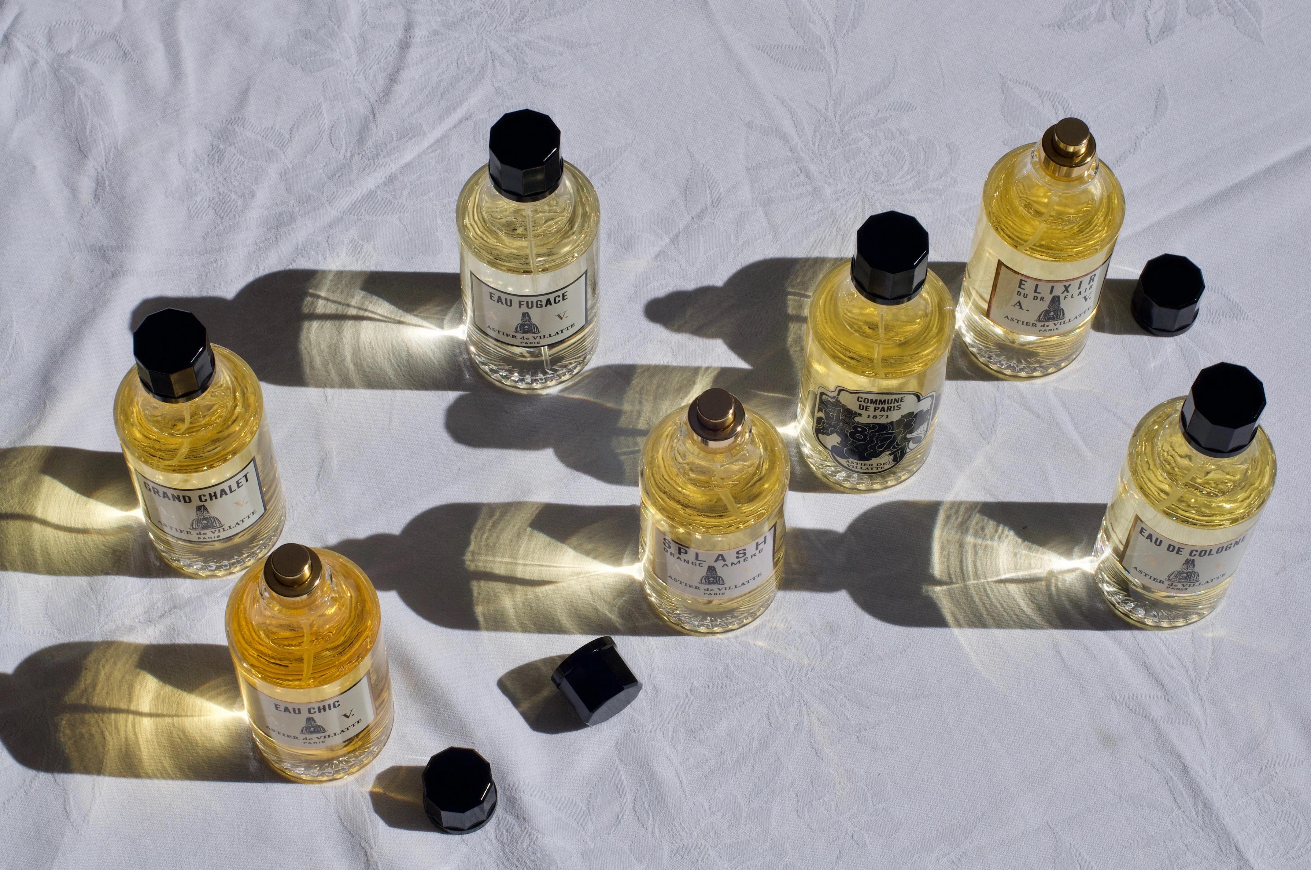 Seven handcrafted glass perfume bottles with black caps arranged on a white surface. Shadows and reflections create interesting patterns.