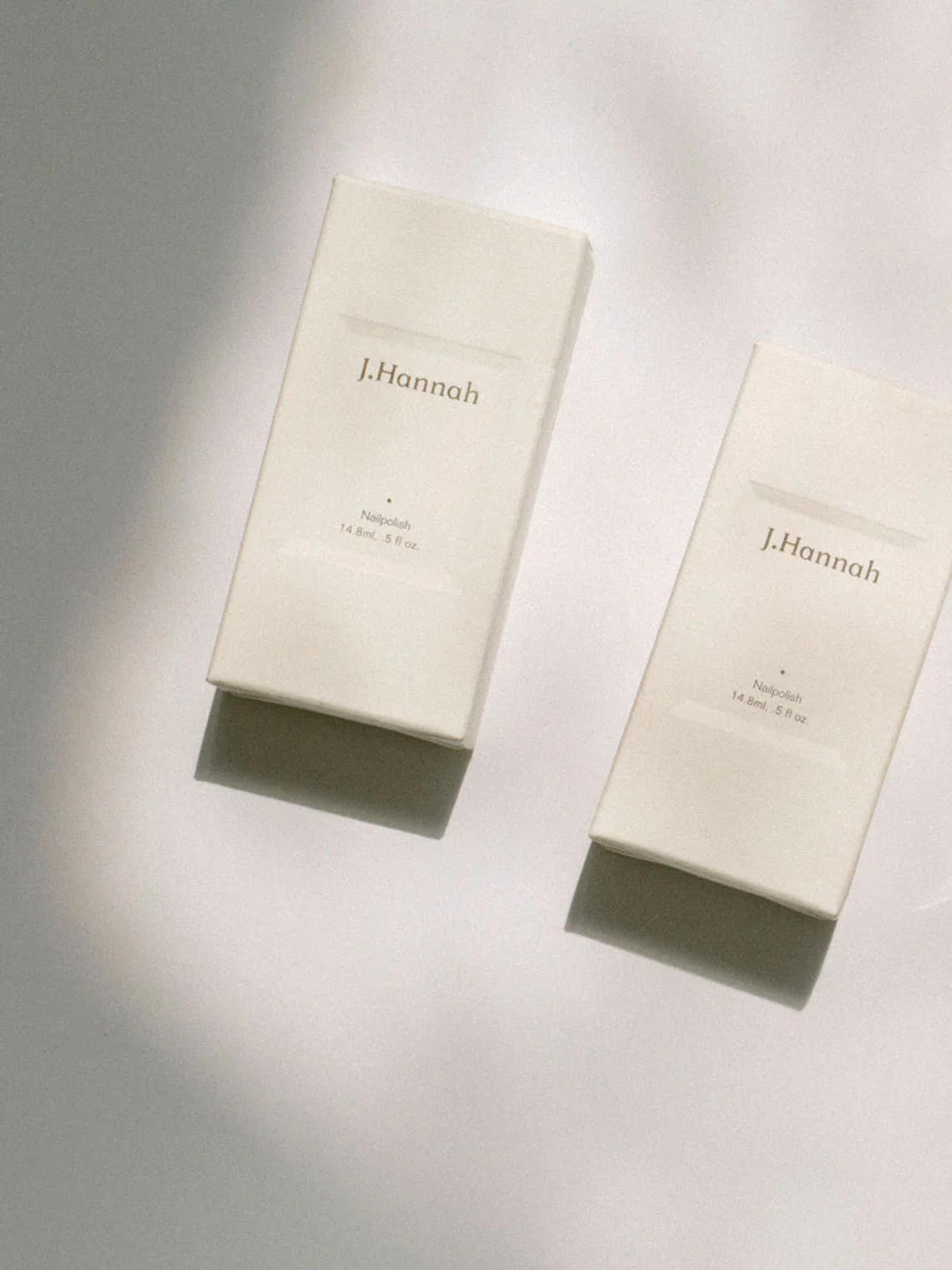 Two white rectangular boxes labeled “J. Hannah” are softly lit against a white background. The minimalist design and warm lighting create a serene ambiance.