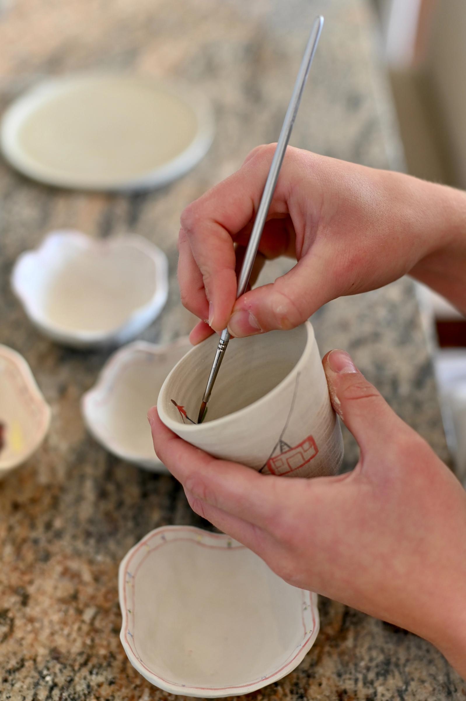 artists hands painting onto ceramic vessel