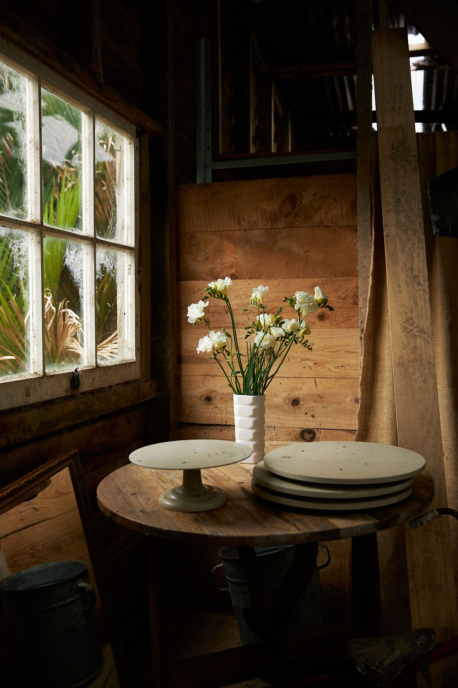 a white vase of white flowers beside a window