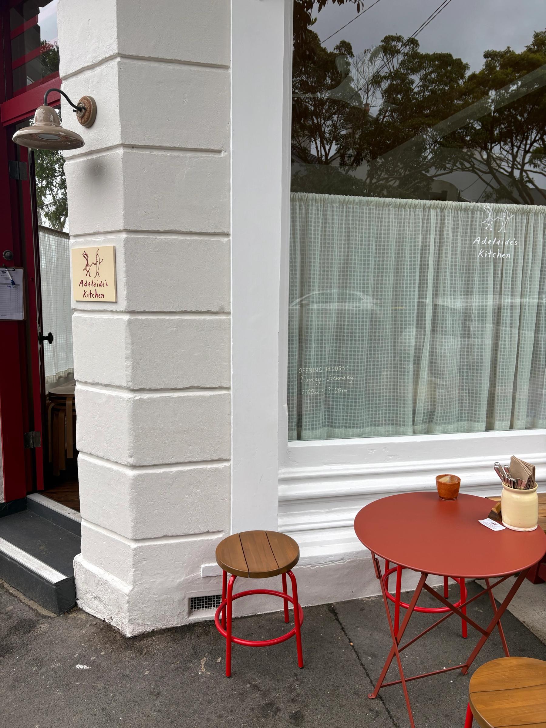 entrance to adelaide's kitchen cafe with red tables and stools outside and a cotton curtain in the window