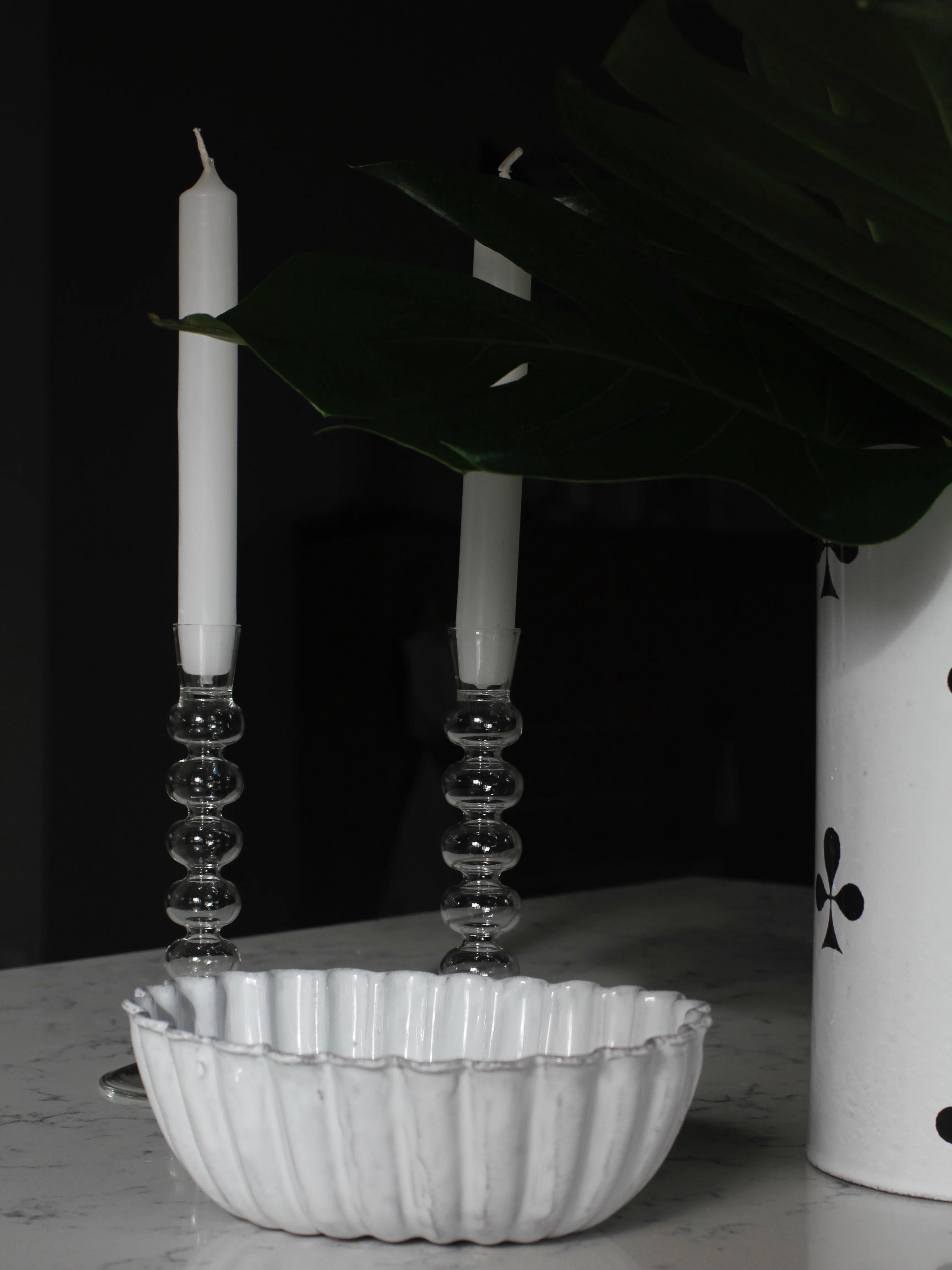 White fluted bowl and vase with black patterns on marble. Astier de Villatte candles glow softly, creating an intimate, moody ambiance.