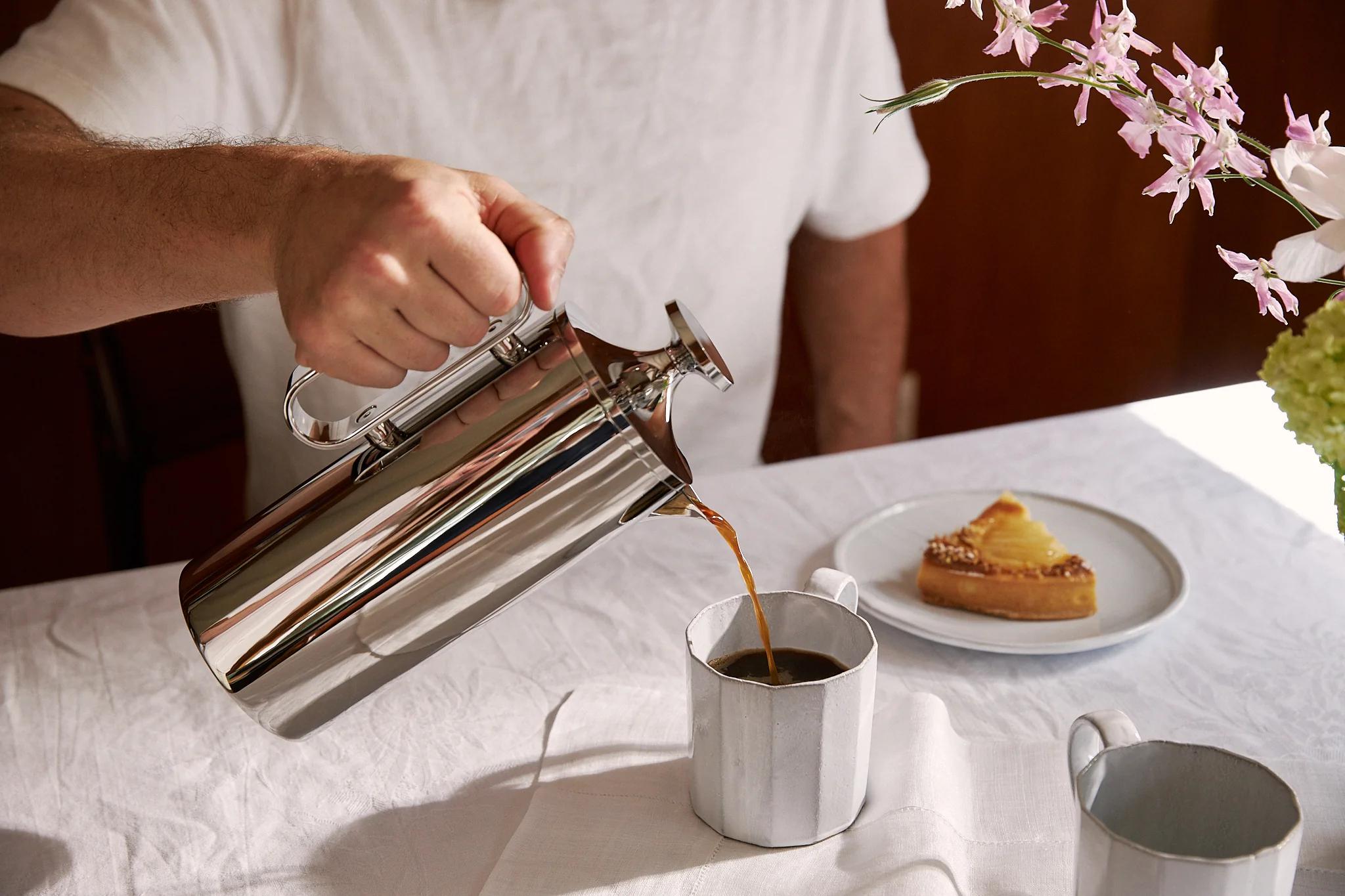 A man pouring coffee from a steel coffee pot into a white coffee cup