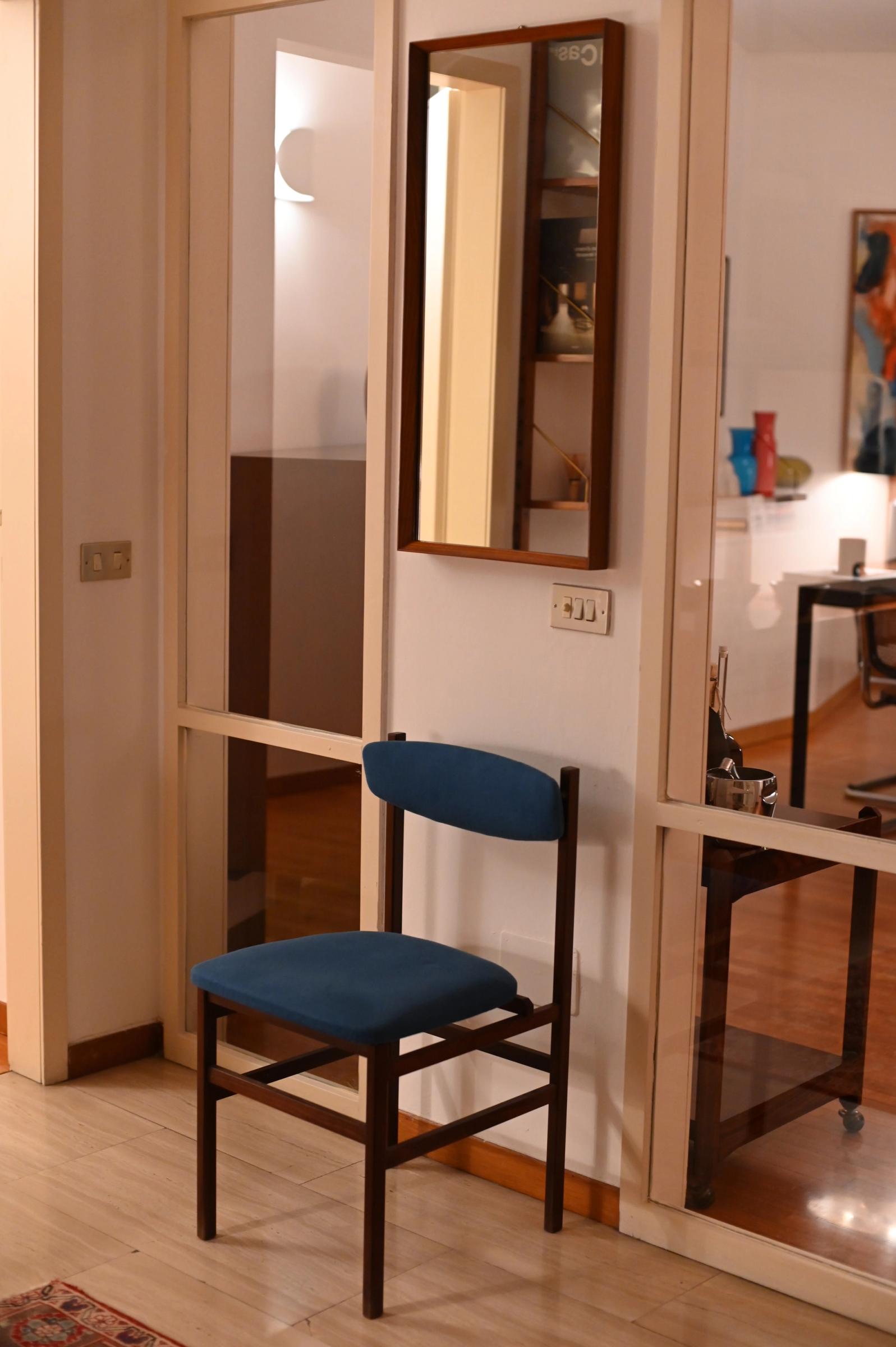 a blue chair under a mirror in the hallways of a home 