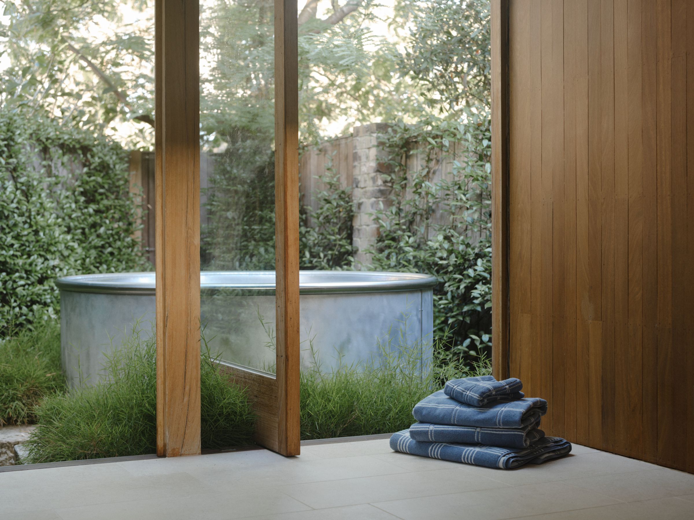 stack of towels sit at the entrance overlooking the silver bath tub outdoors 