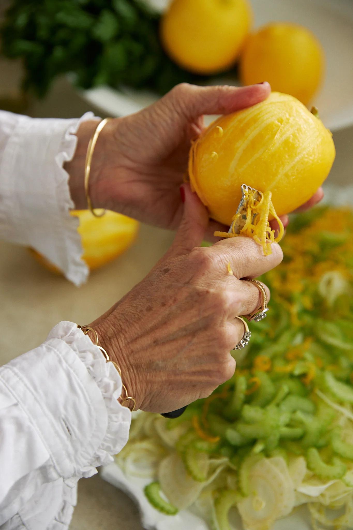 woman zests a bright lemon over a platter of salad ingredients