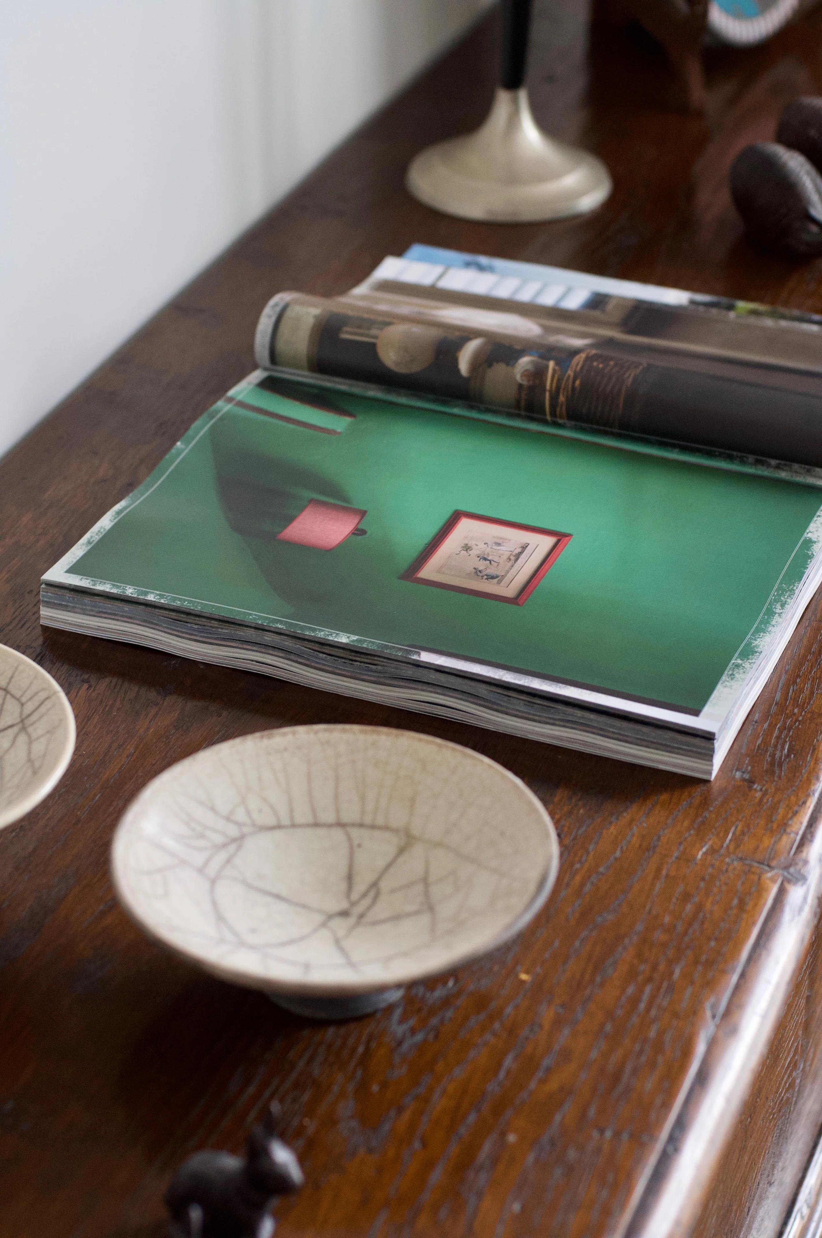 Open CABANA Magazine showing green room photo. Ceramic bowls, candle holder, and animal-shaped ornament on table.