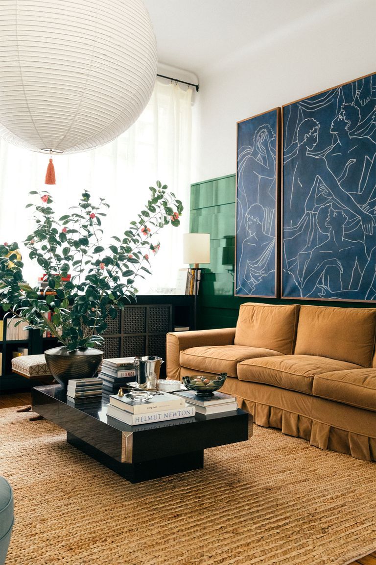 Living room with mustard couch, wooden coffee table, blue art pieces. Balthus Lamp hanging, illuminating sisal rug.