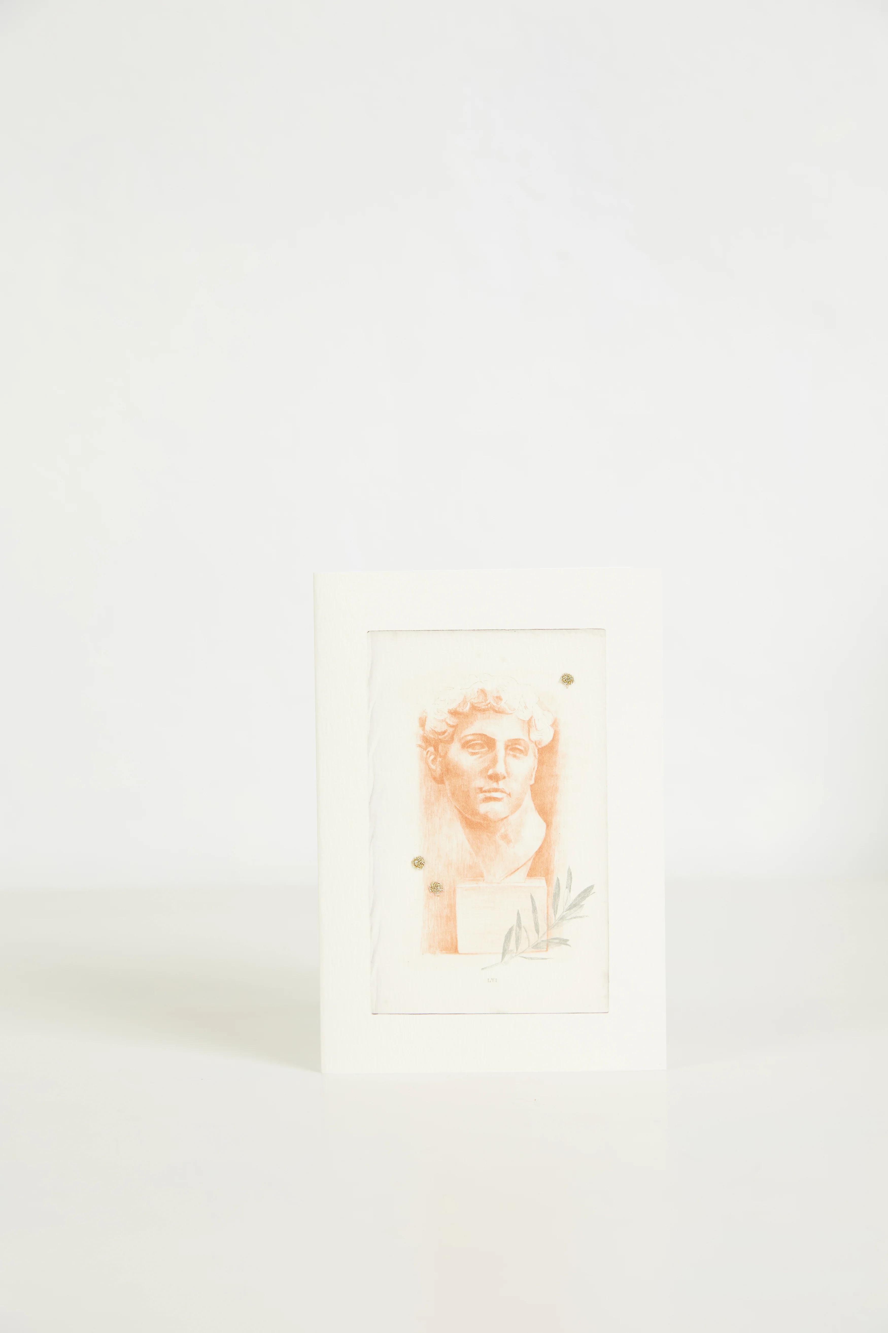 A greeting card with a monochromatic illustration of a classical bust in soft orange tones with floral designs at the base. The card is upright against a white background.