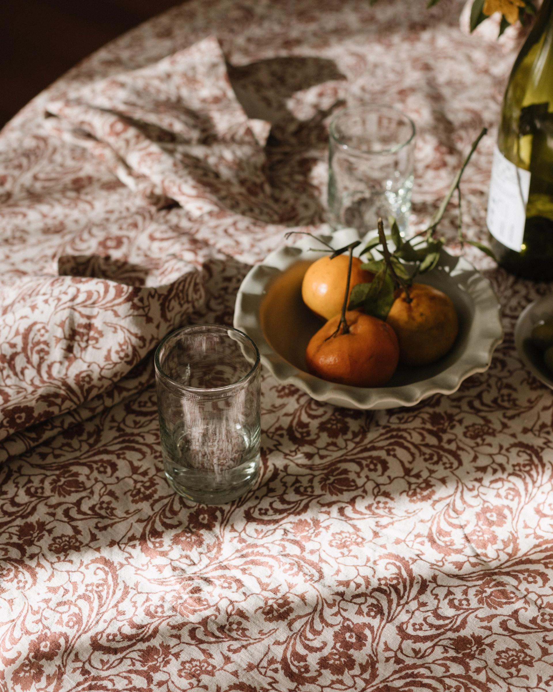 light falls over a cream and red tablecloth with a bowl of tomatoes
