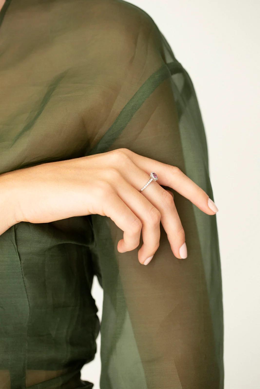 Close-up of hand with diamond engagement ring. Sheer dark green blouse visible. Elegance of Charlotte Penman jewellery evident.