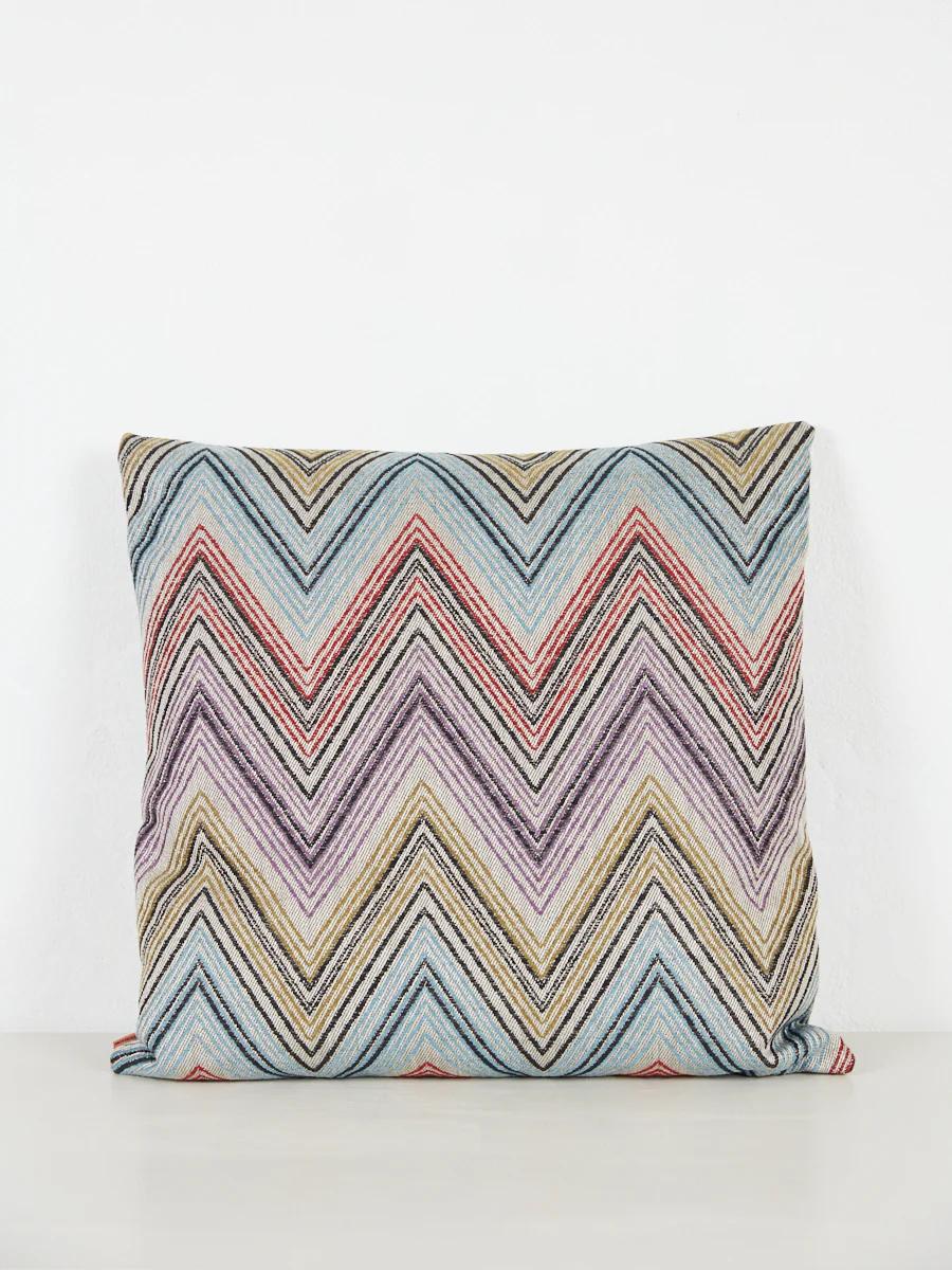 Square pillow with detailed chevron pattern. Light blue, red, purple, yellow, black mix. White background.