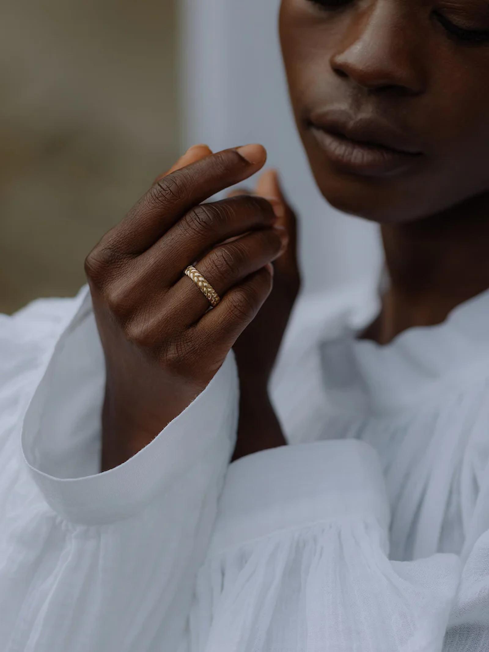 Close-up of dark-skinned person in white garment. Gold textured ring with gemstones on middle finger.