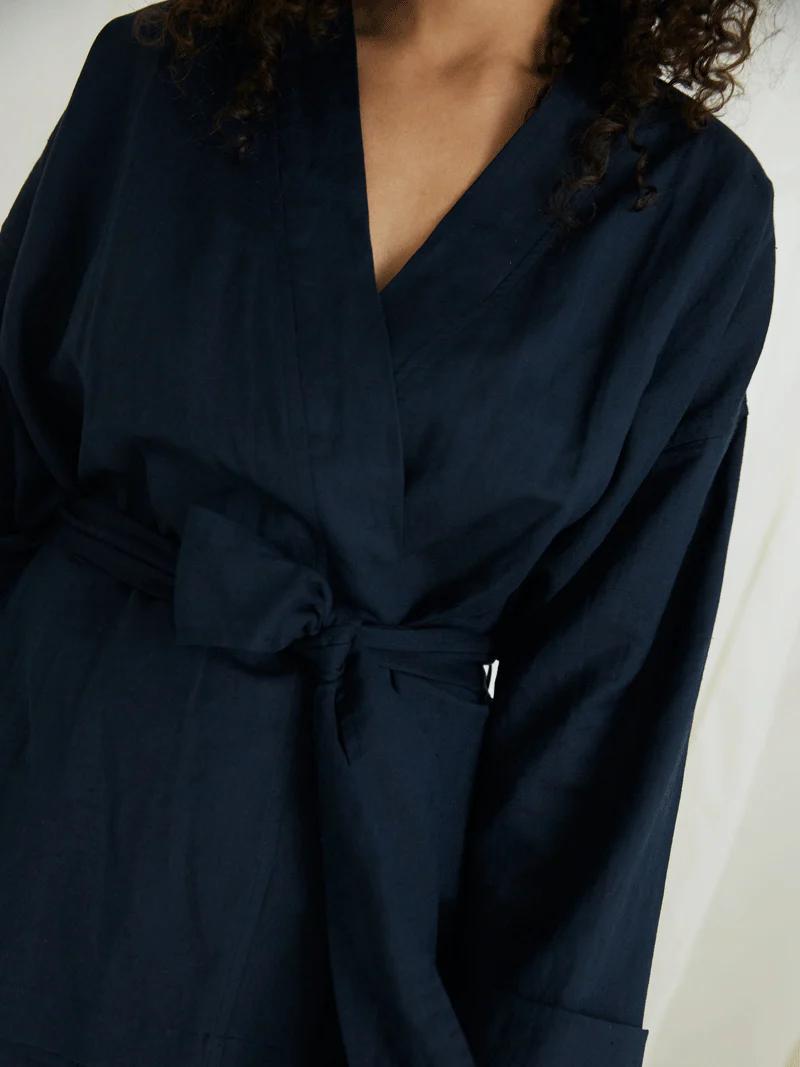 Close-up of person in navy blue wrap robe. Curly hair visible. Showcases sustainable sleepwear details.