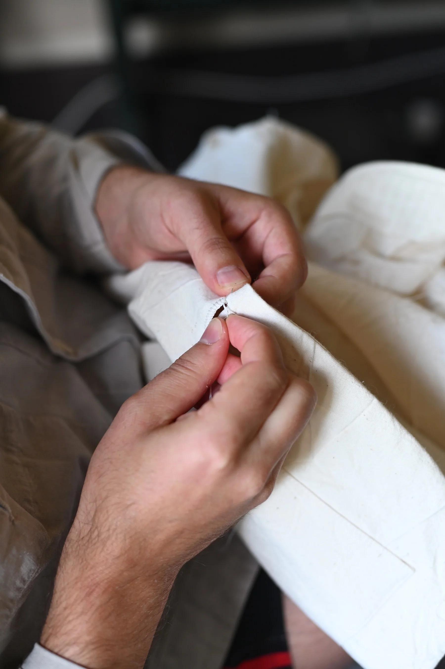 Close-up of hands sewing white fabric. Light grey shirt visible.