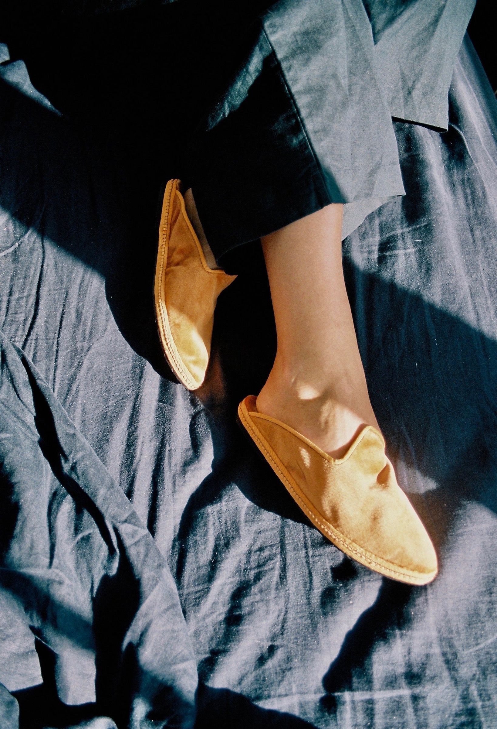 Close-up of tan slip-on shoes on a textured fabric with sunlight casting shadows, evoking the ocean’s rhythmic waves in a seaside cottage.