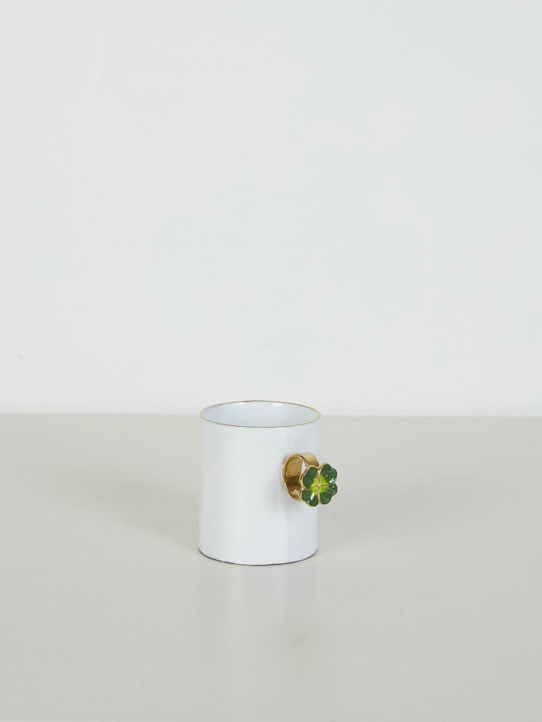 White mug with gold fruit-shaped handle and green leaf. Light-coloured surface, white background.