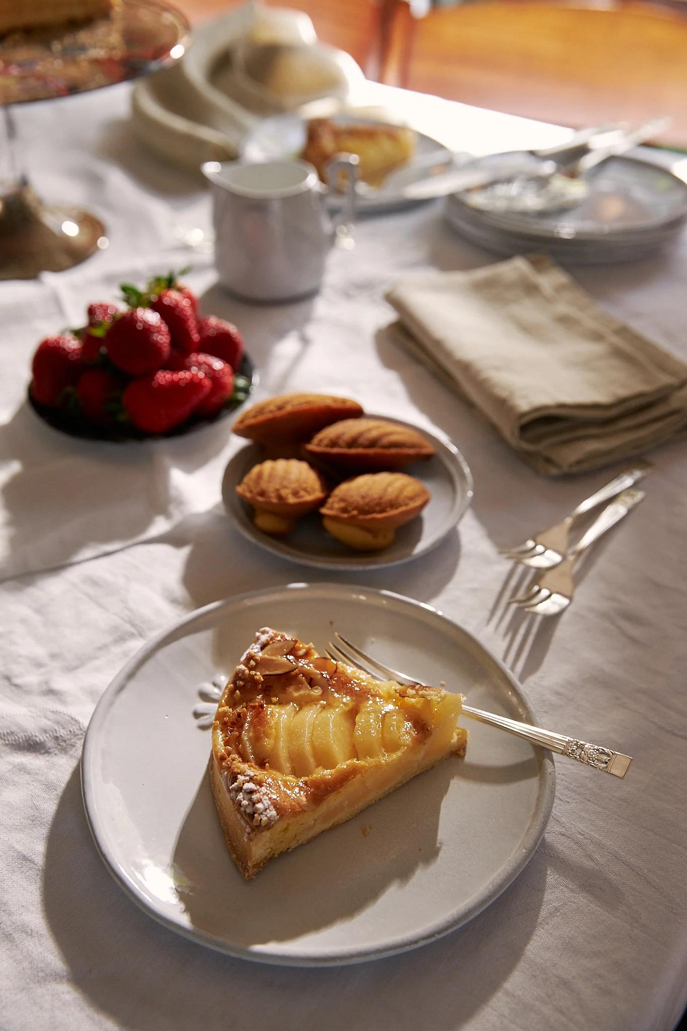 A slice of pear tart sits on a white place in the sunlight