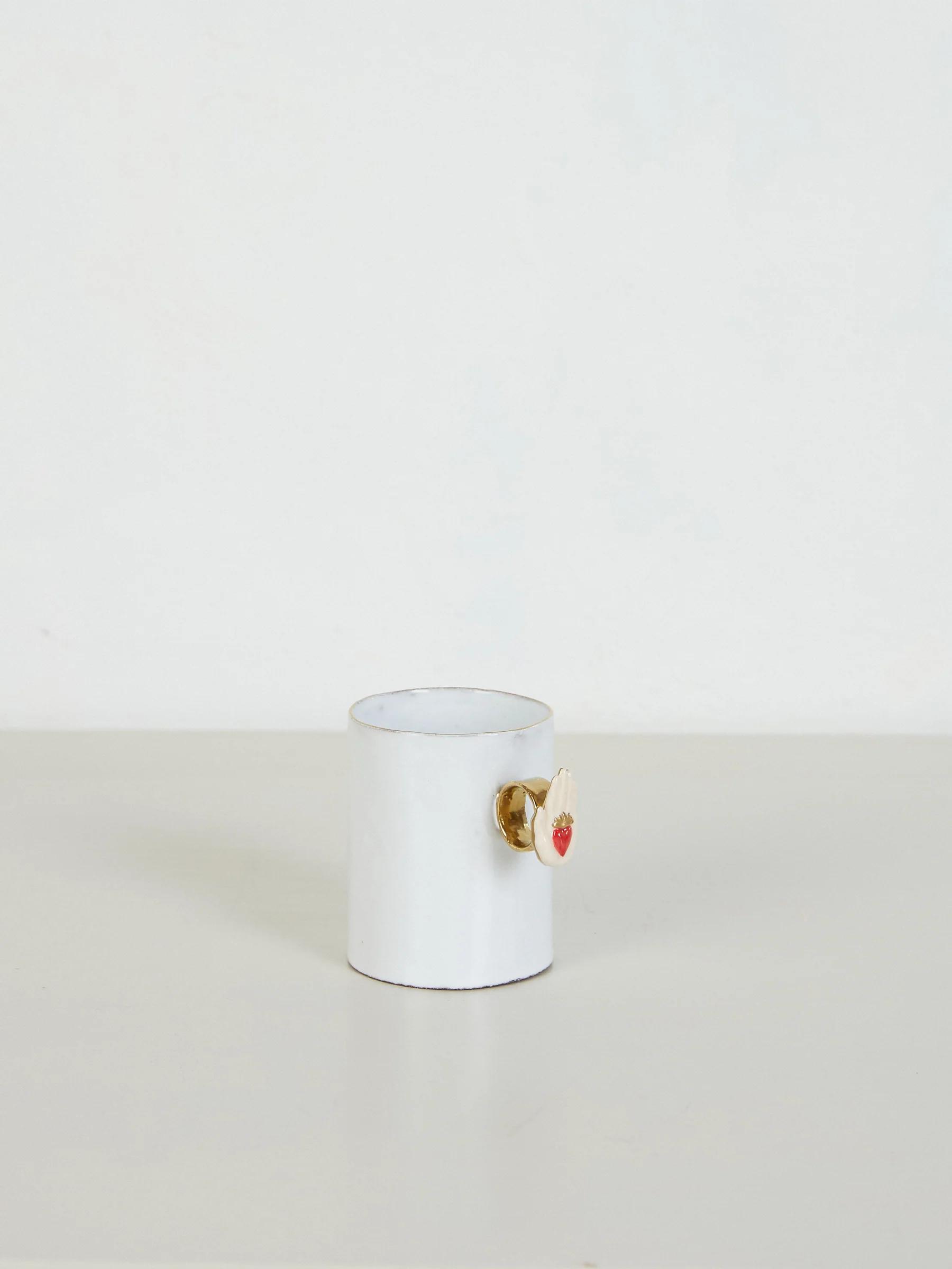 White ceramic mug with small floral-shaped handle. Pink centre on handle. White surface and background.