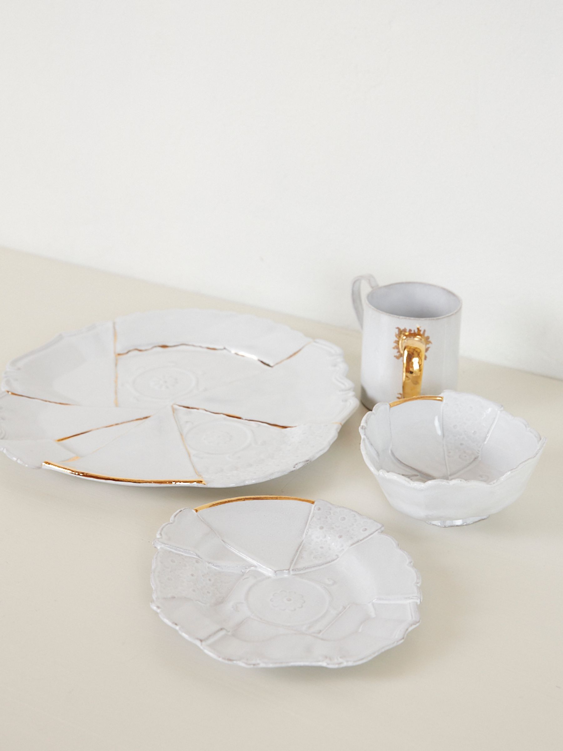 one large plate and one small plate sit next to a white bowl and gold accented mug