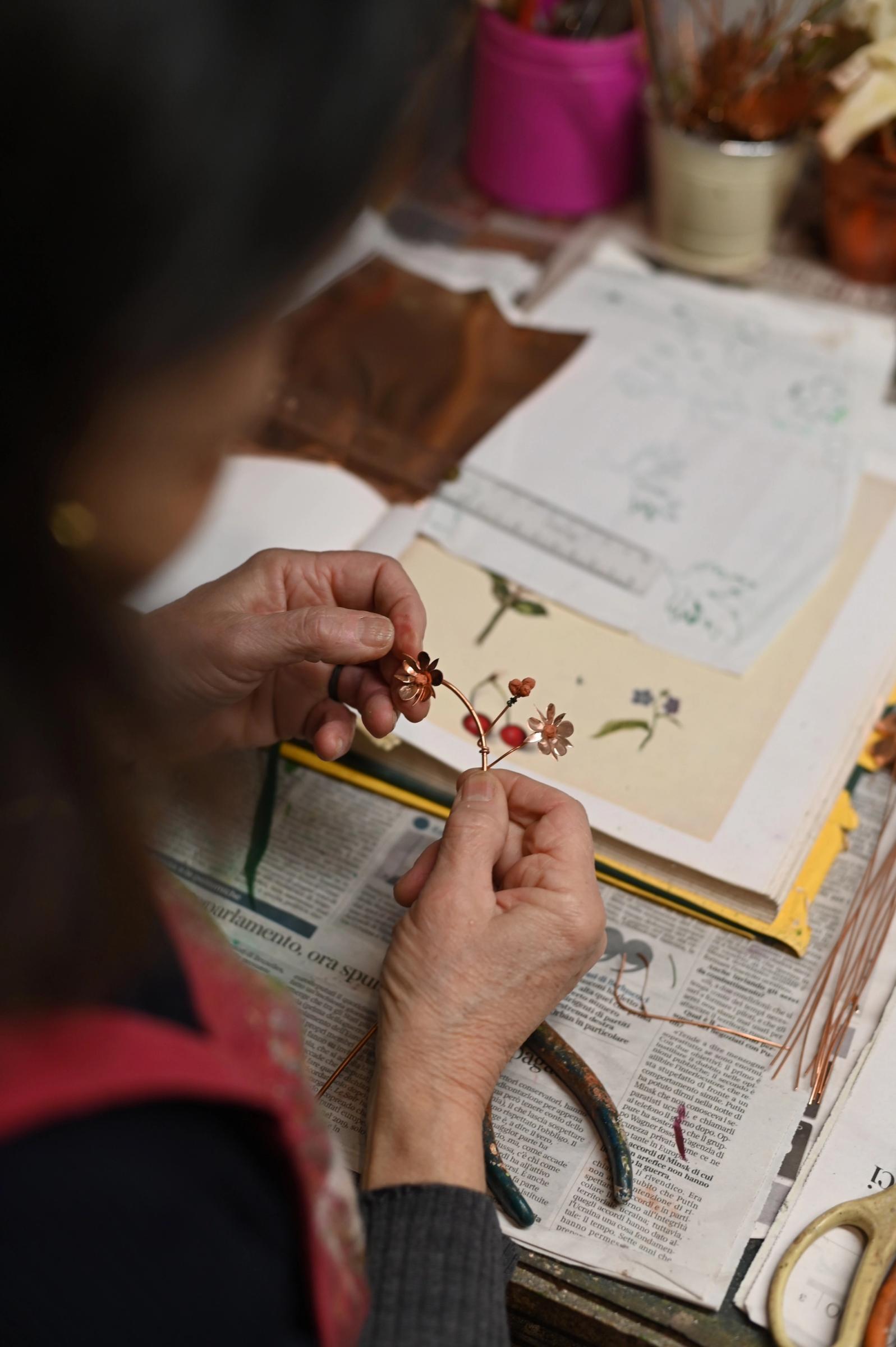 Laura holds copper flowers in her hands at workbench