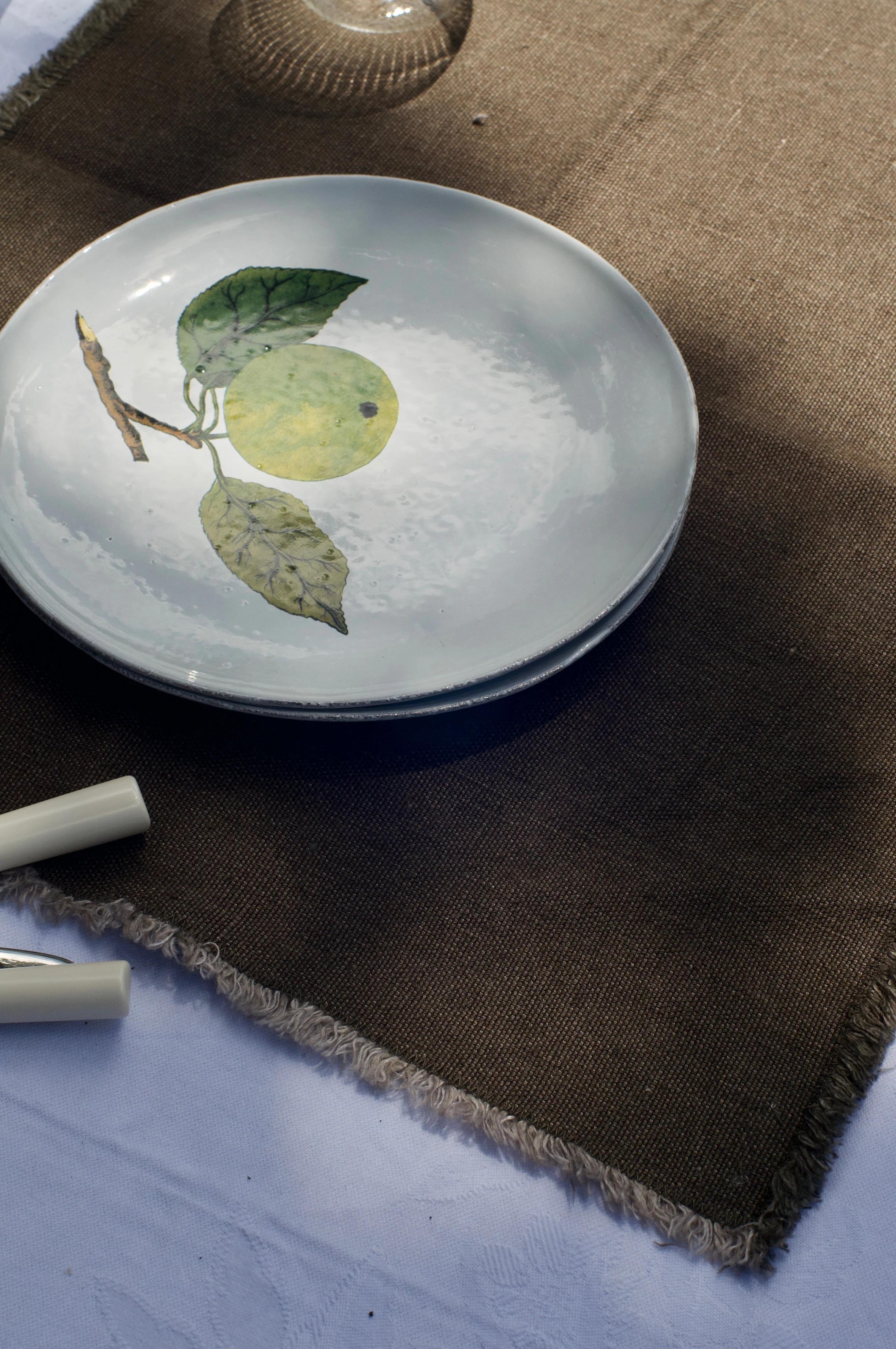 White plate with lemon design on brown placemat. Wine glass and candles visible. Natural light setting.