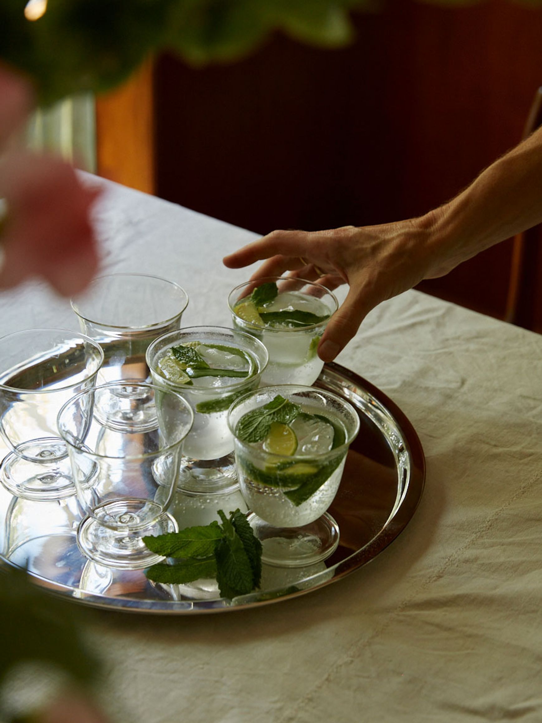 Glasses on silver tray with hand reaching for one of them in natural light