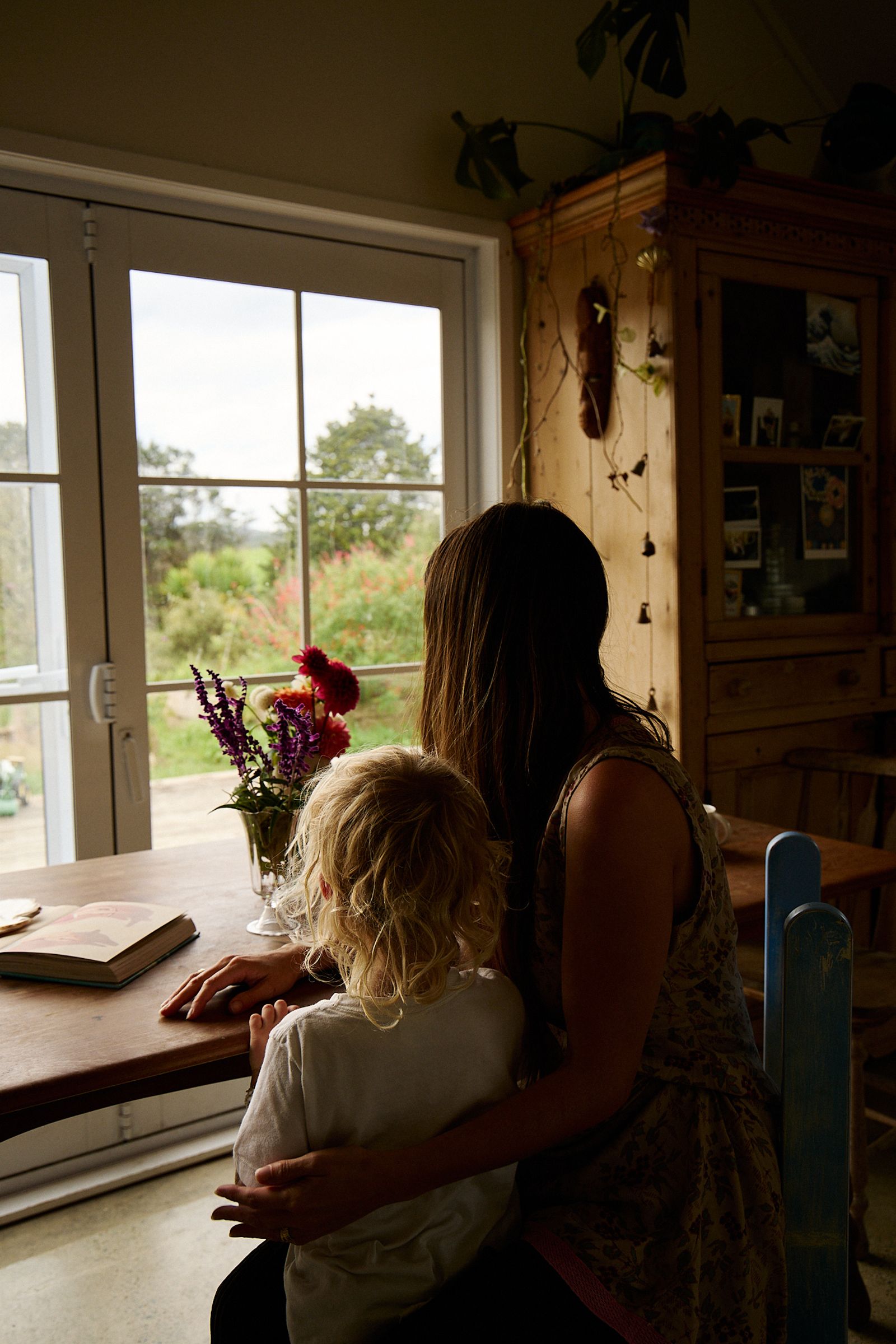 mother and son sit at dining table overlooking their garden 
