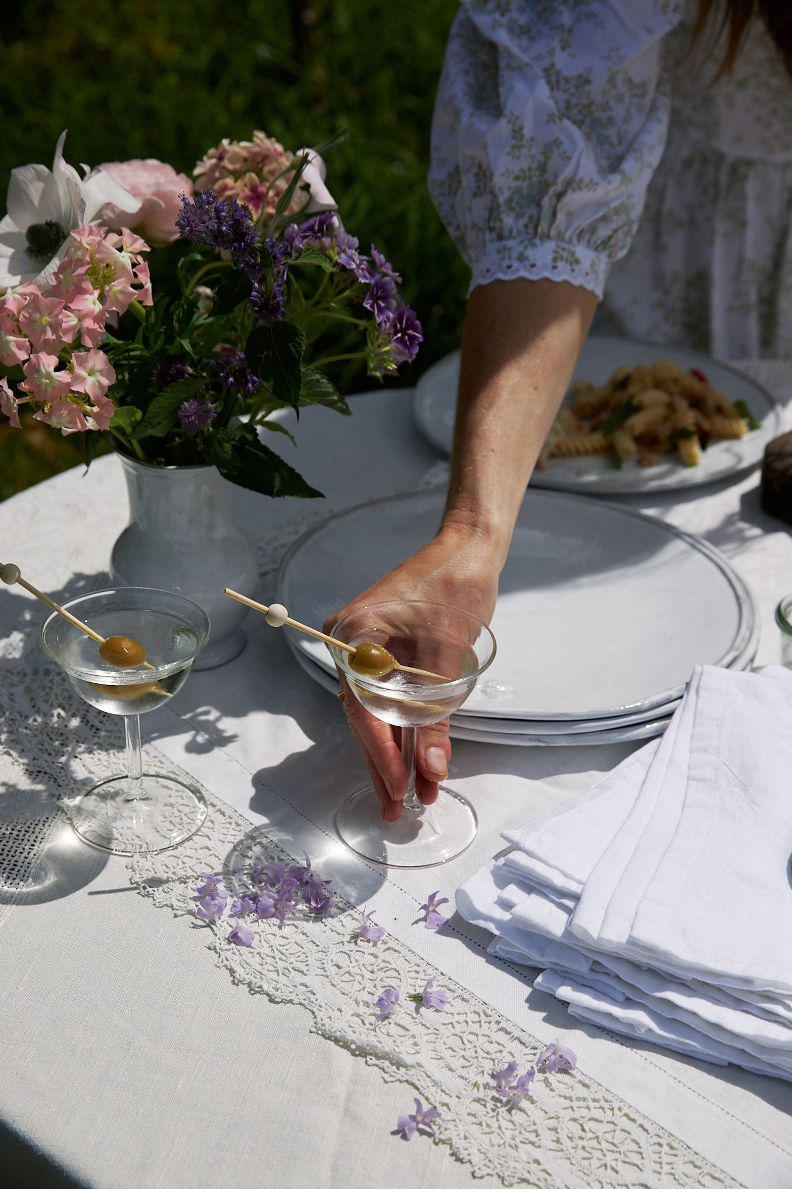 woman places a cold martini and olive down onto tablecloth in the sun