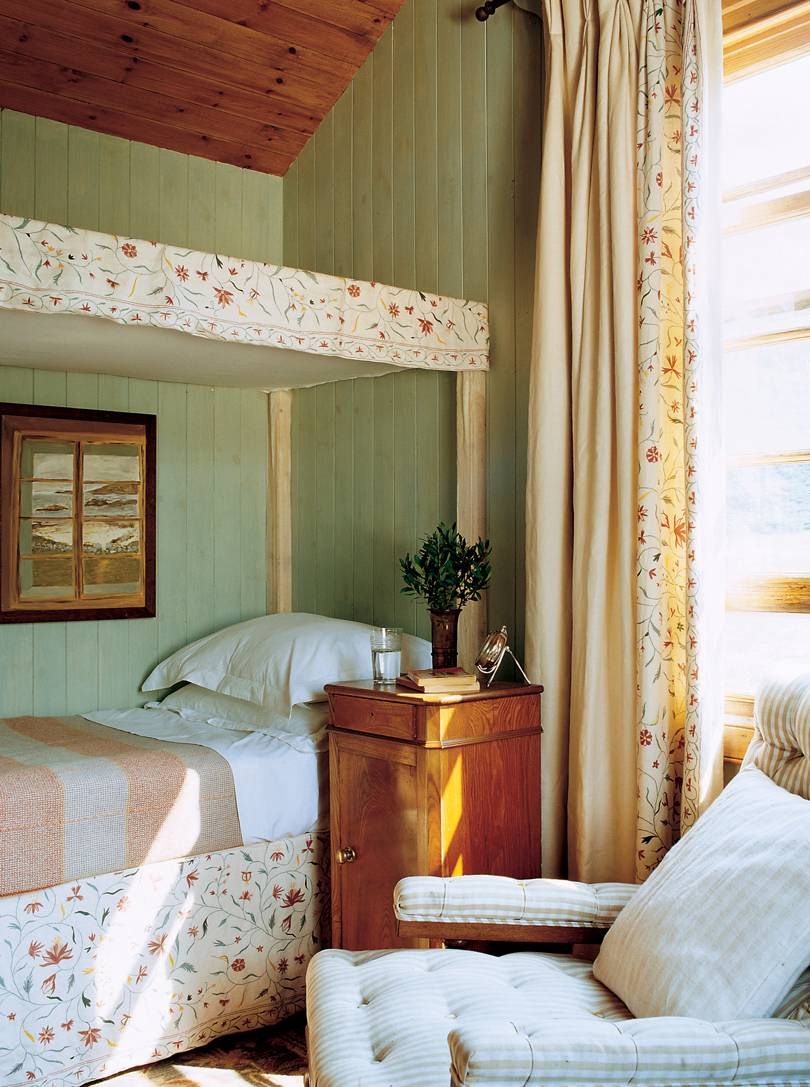 Jura holiday bedroom with green walls. Floral bedding, nightstand with plant. Chair under window with floral curtains.