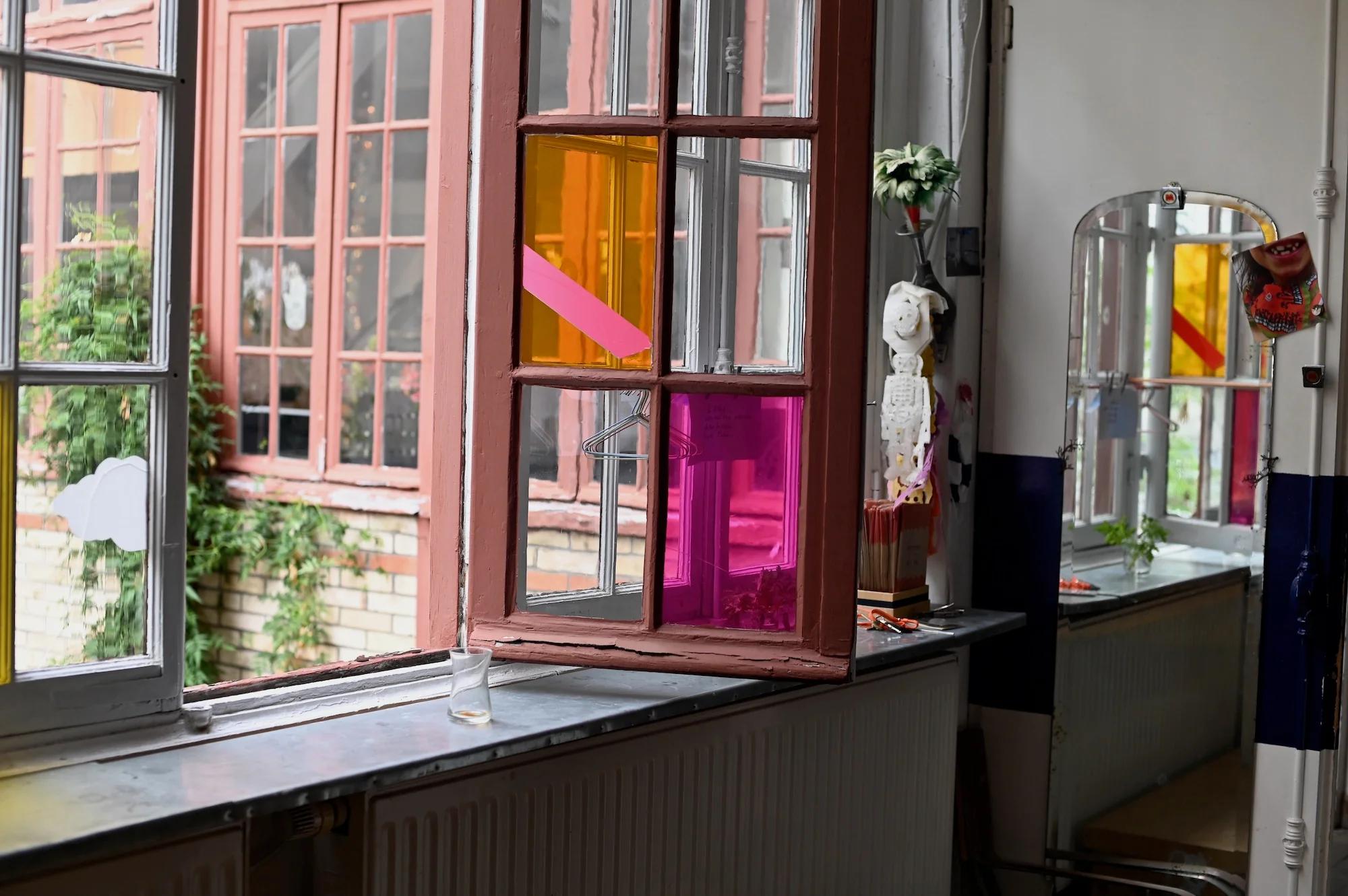 Colourful window panes let light into eclectic room. Plants outside. Mirror reflects room's art and plants.