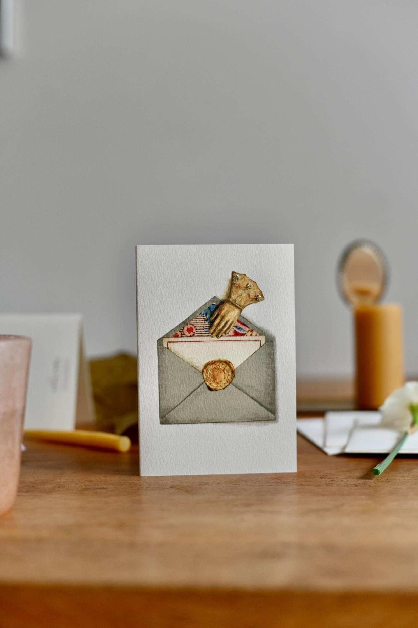 A greeting card with a drawing of an antique hand and envelope. The card stands against a plan white background.