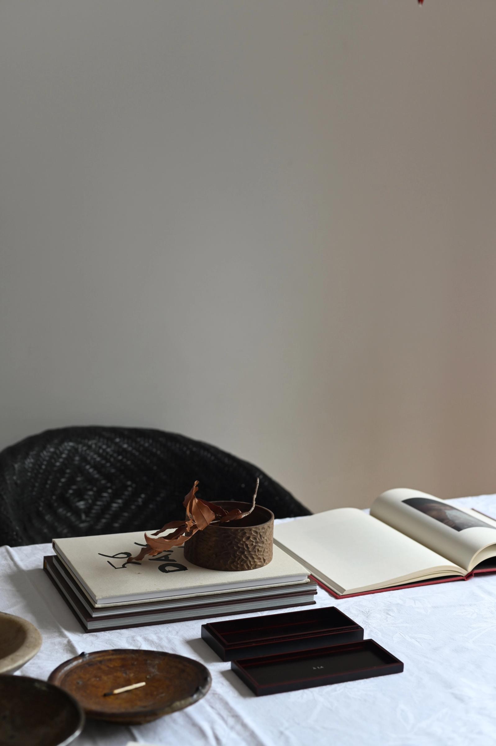 table scene of incense box, books, a black chair and ceramic bowls