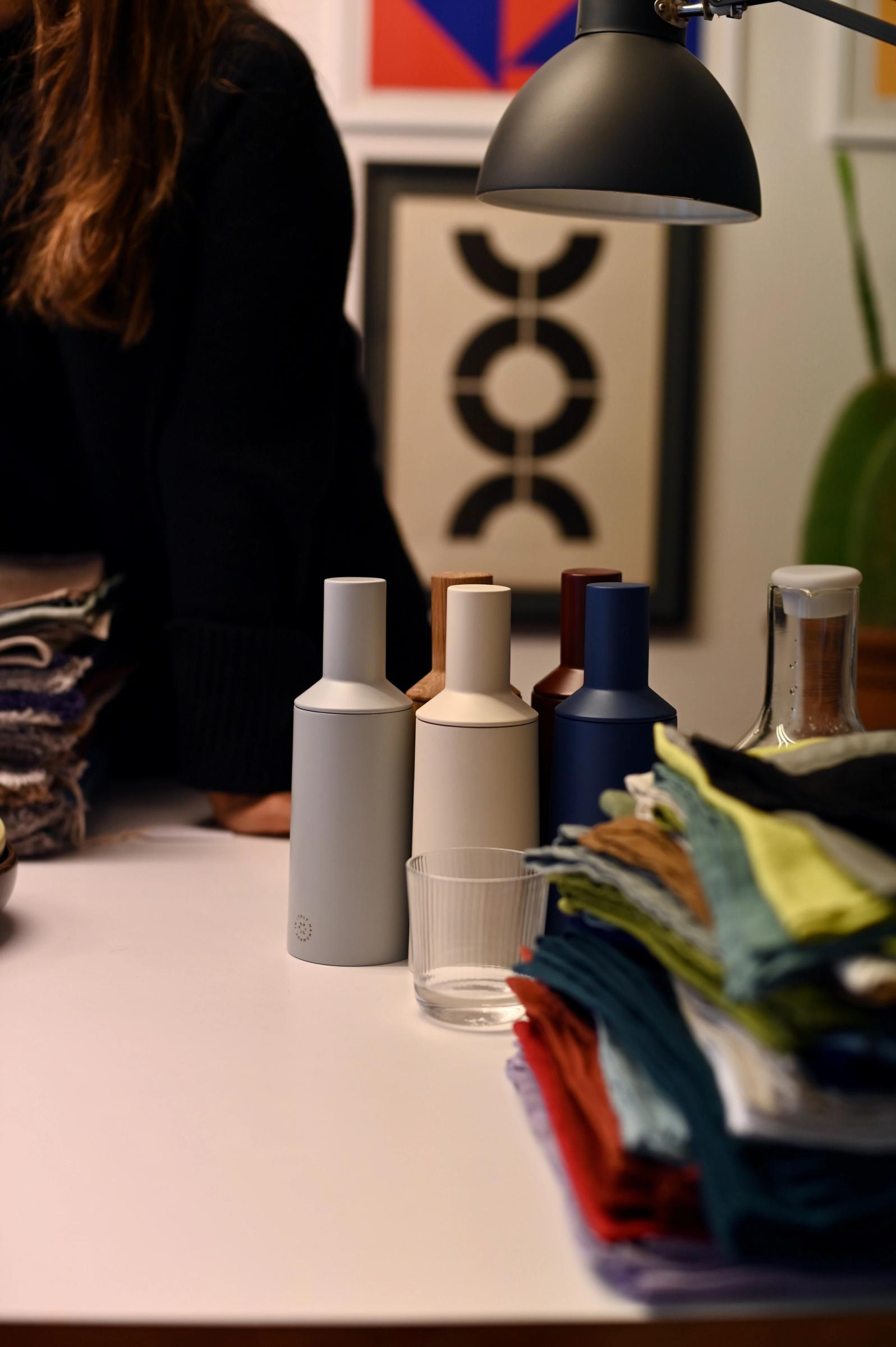 coloured pepper mills sit bunched on a desk in front of a graphic print