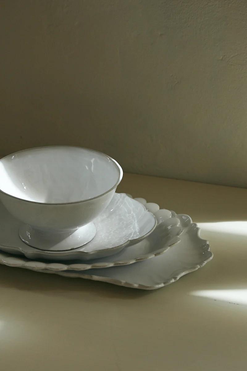 Stacked white ceramic tableware on off-white surface. Bowls on various shaped plates. Soft light, pale background.