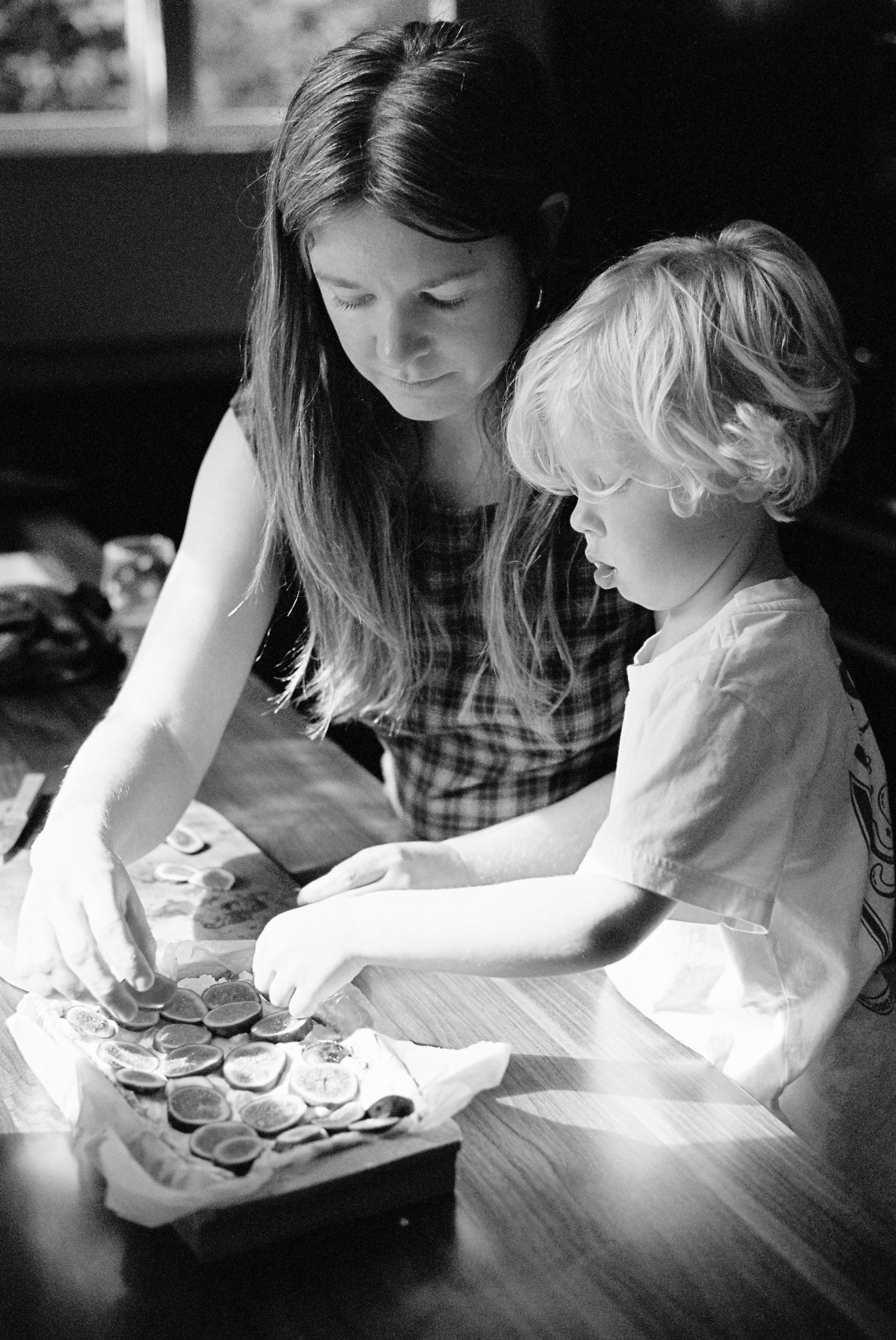 Black and white photo of children arranging fruit on tray. Sunlit midcentury home setting.